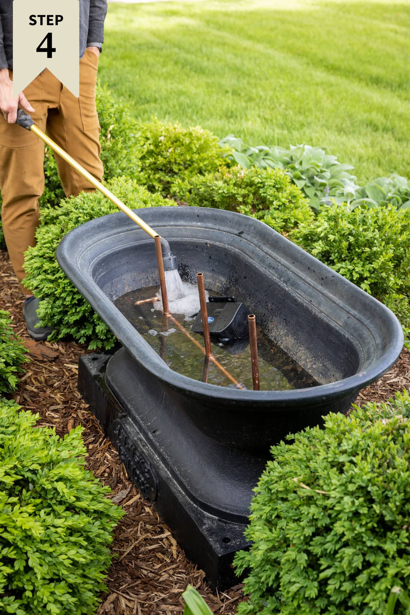 Man filling up a black cast iron DIY water fountain with a hose with copper fountain.