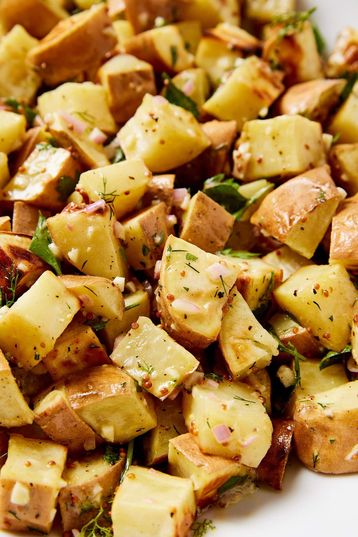 Chunks of diced sweet potato covered in a homemade vinaigrette with mustard seeds and fresh herbs.