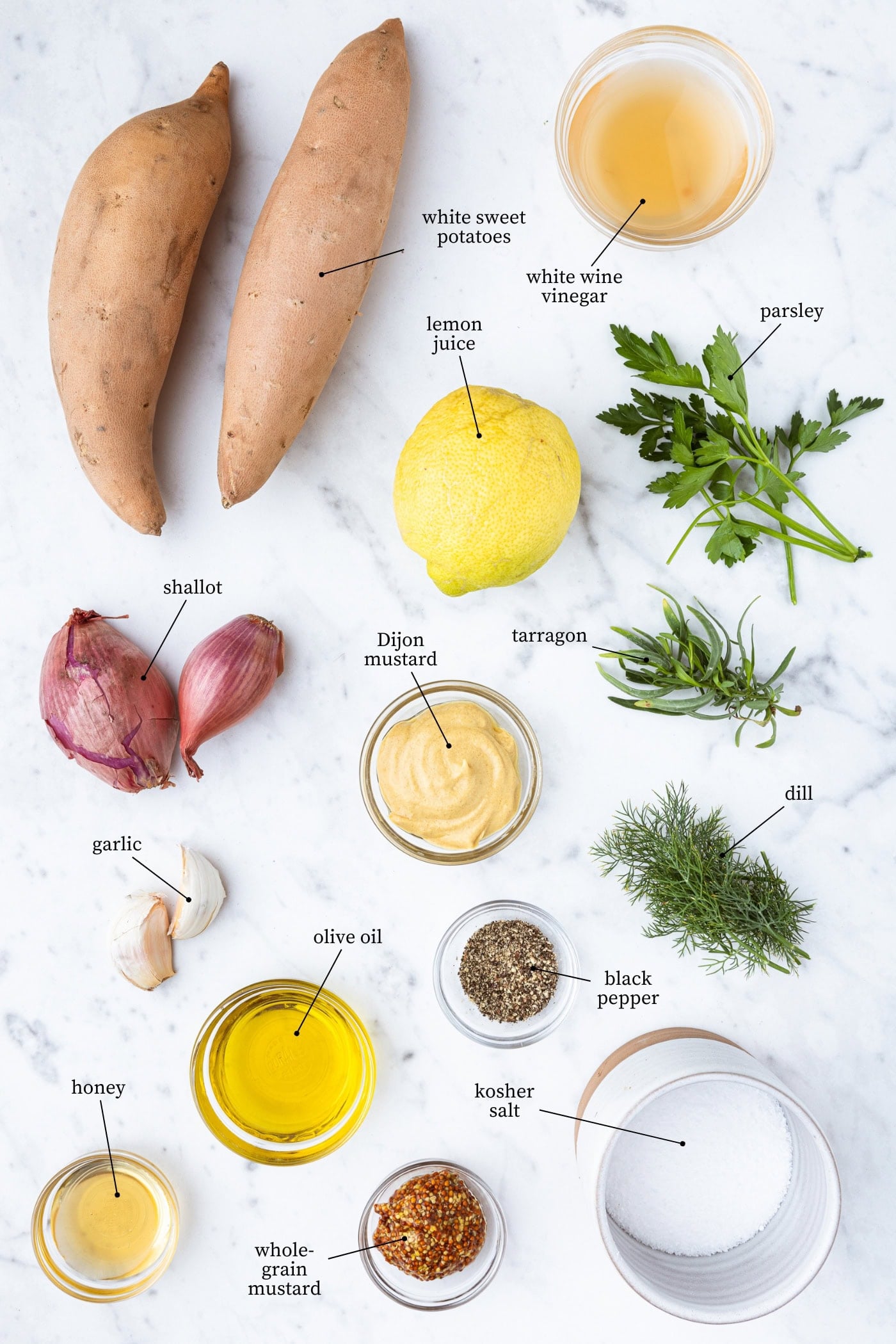 White marble surface filled with all ingredients for French potato salad including sweet potatoes, shallot, mustards, fresh herbs, spices, and more.
