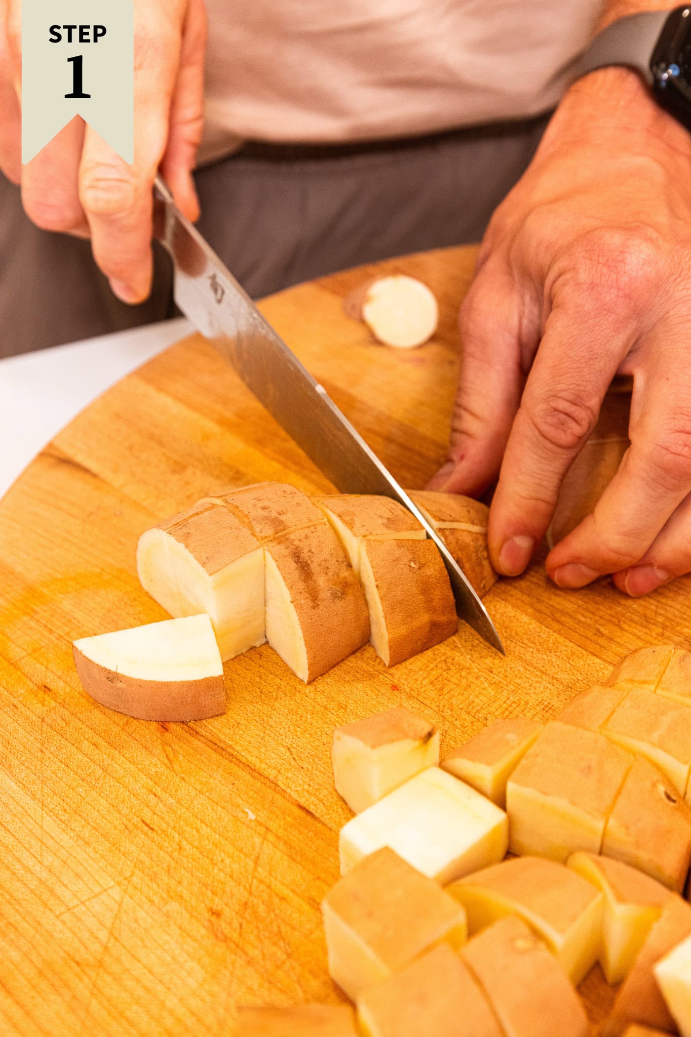 Hand slicing up chunks of white sweet potato on a wooden cutting board.