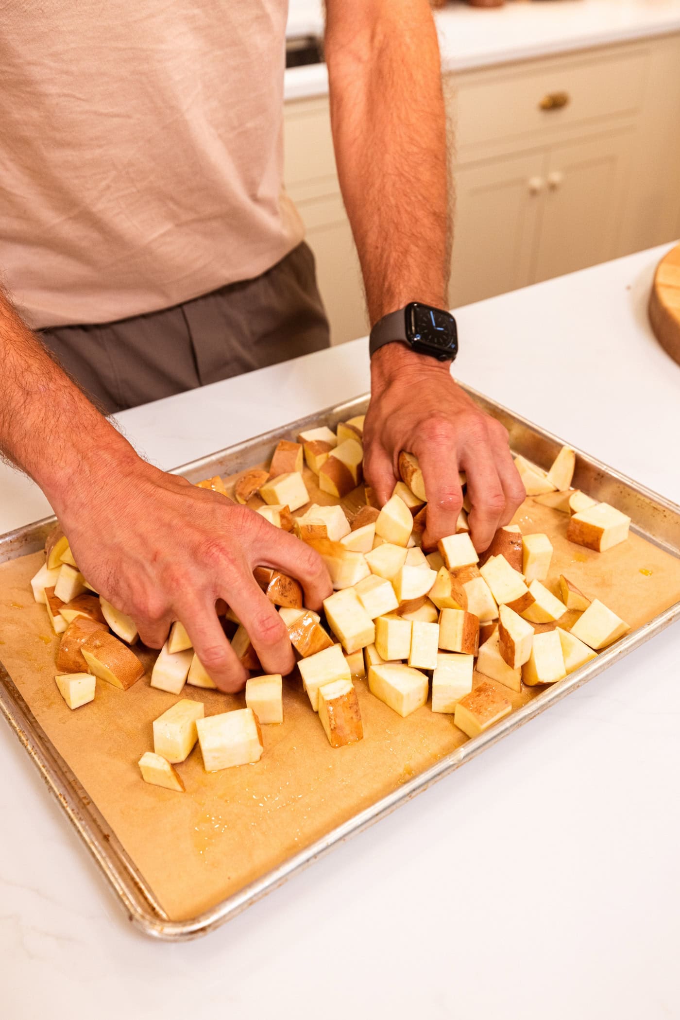 Two hands mixing together diced sweet potatoes with olive oil, salt, and black pepper on sheet pan.