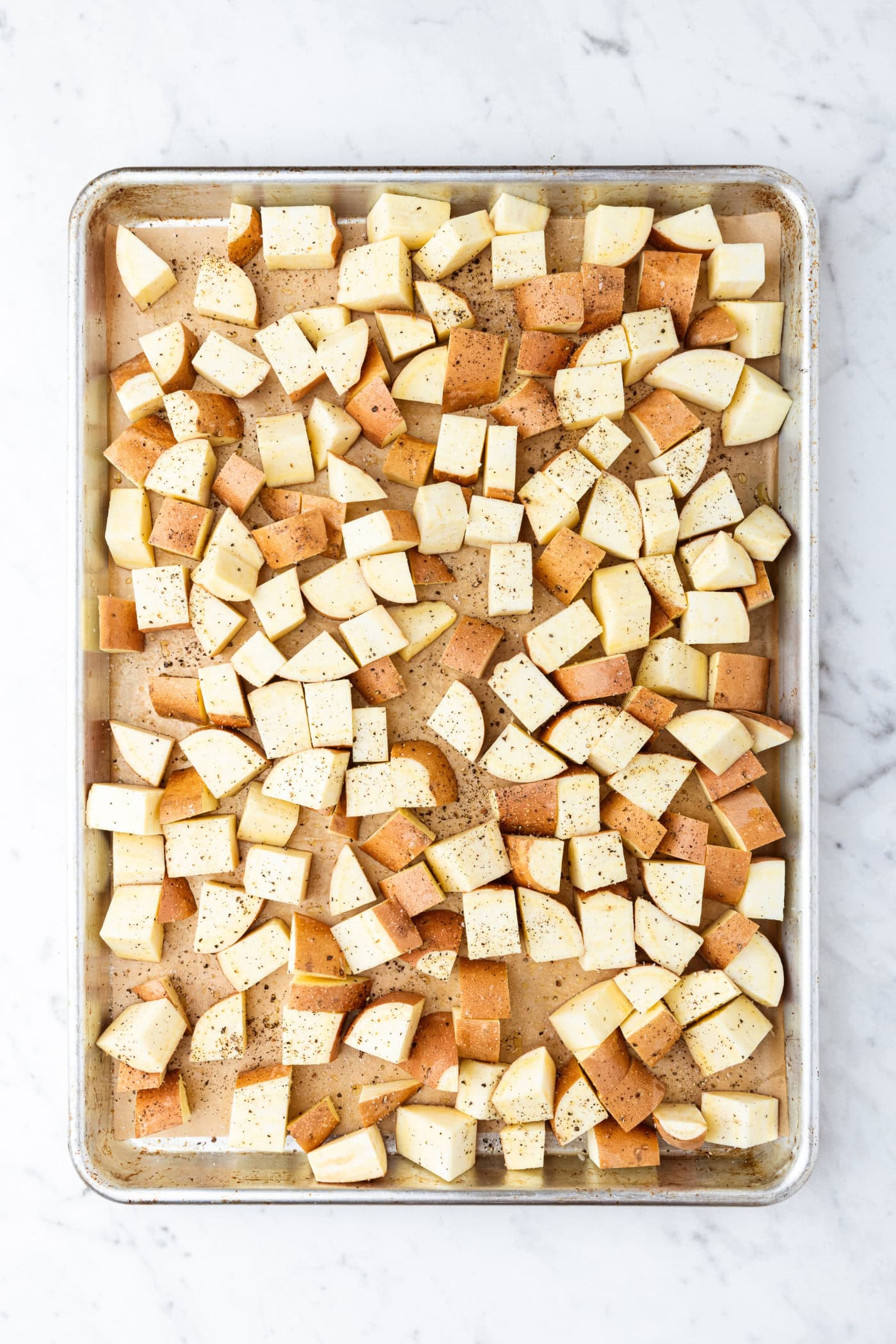 Large metal sheet pan with uncooked raw diced sweet potatoes.