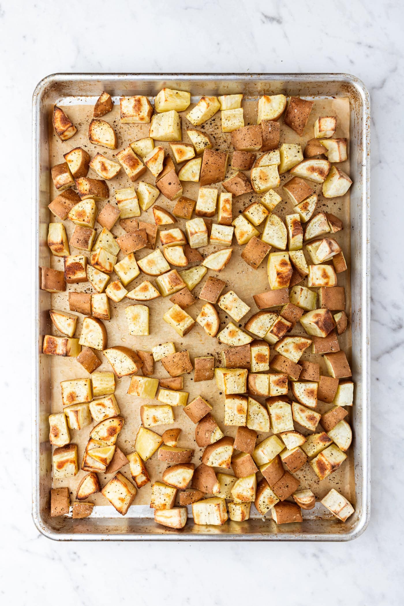 Metal sheet pan with roasted sweet potatoes diced into small cubes right after coming out of the oven.