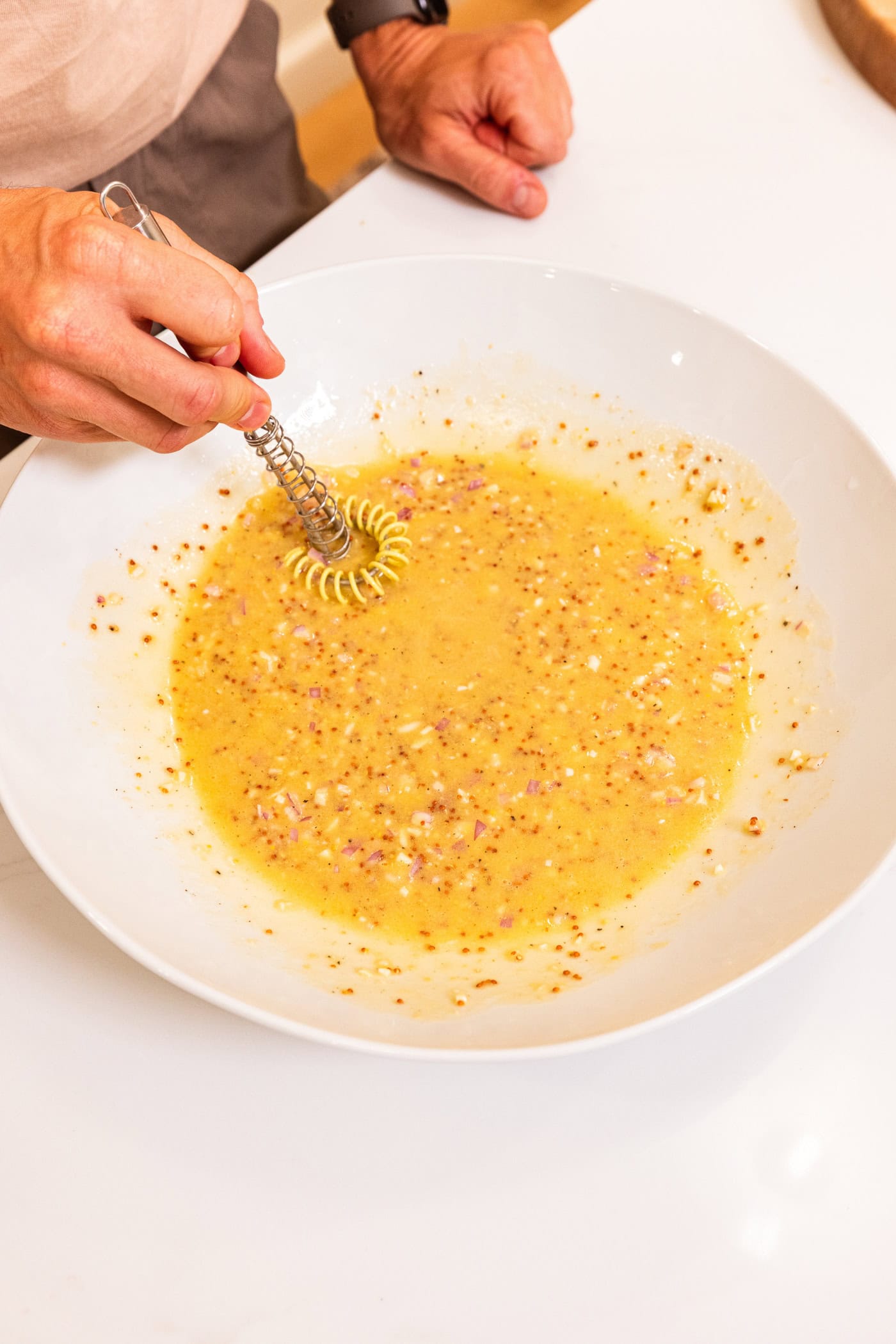 Hand using small whisk to mix together a vinaigrette with a salad.