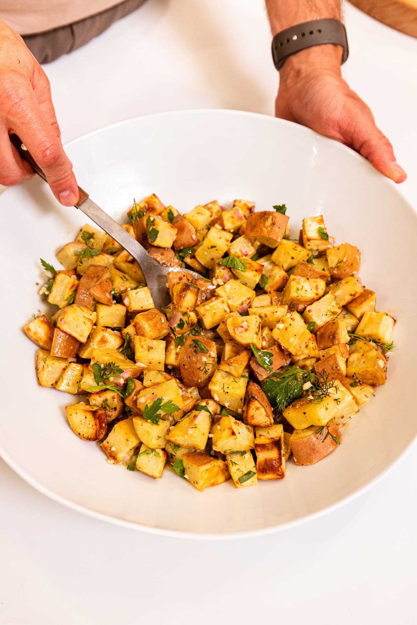Large white serving bowl filled with French-style potato salad with herbs sprinkled all over the top.