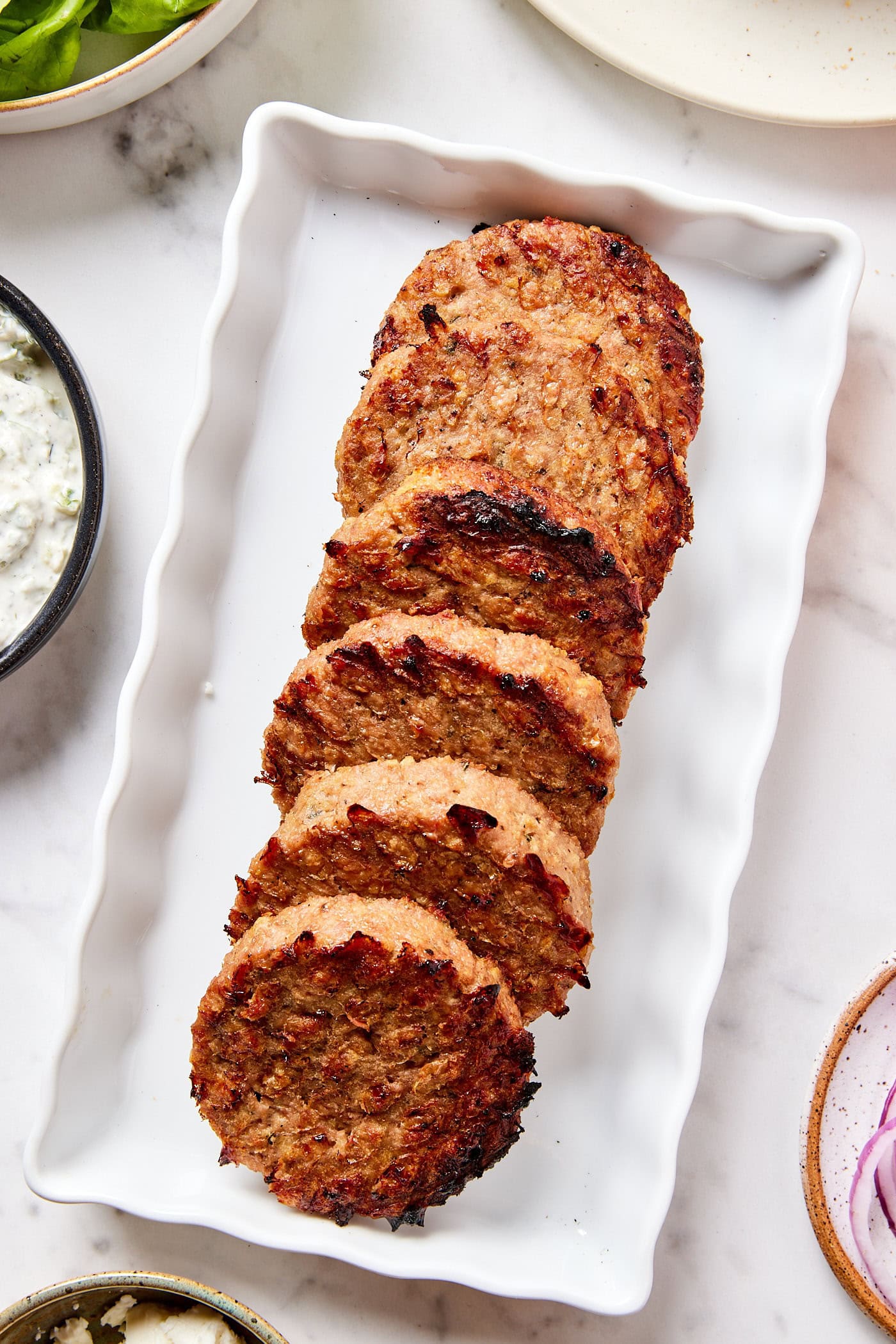 White rectangular platter filled with grilled turkey burgers with charred edges ready to be served.