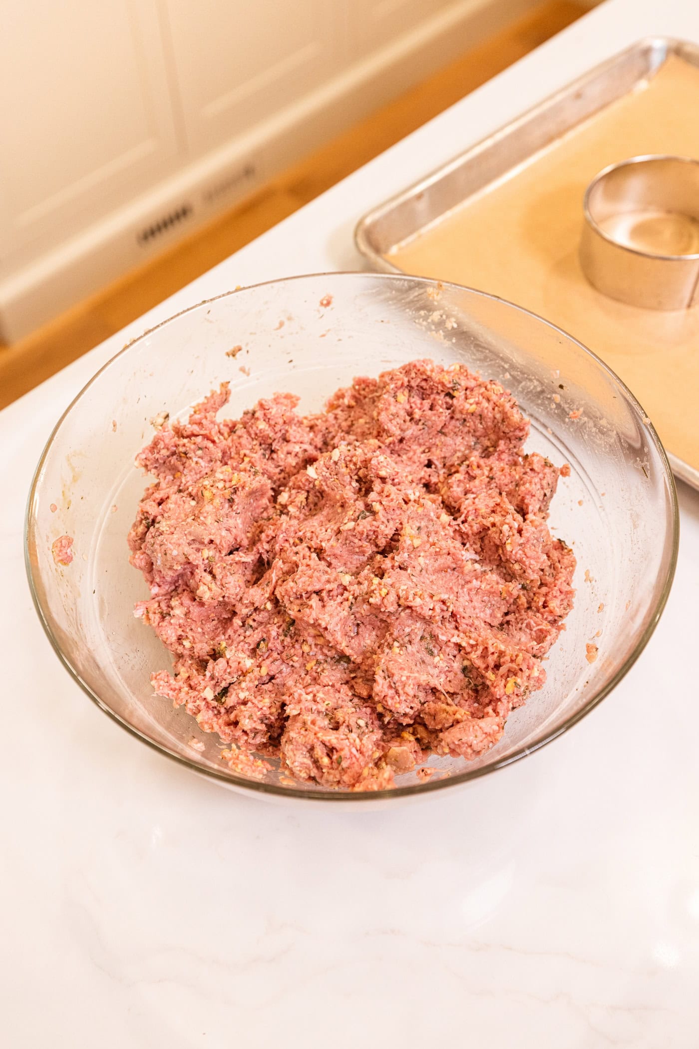 Glass bowl filled with mixed together mixture of ground turkey to form burger mixture for patties.
