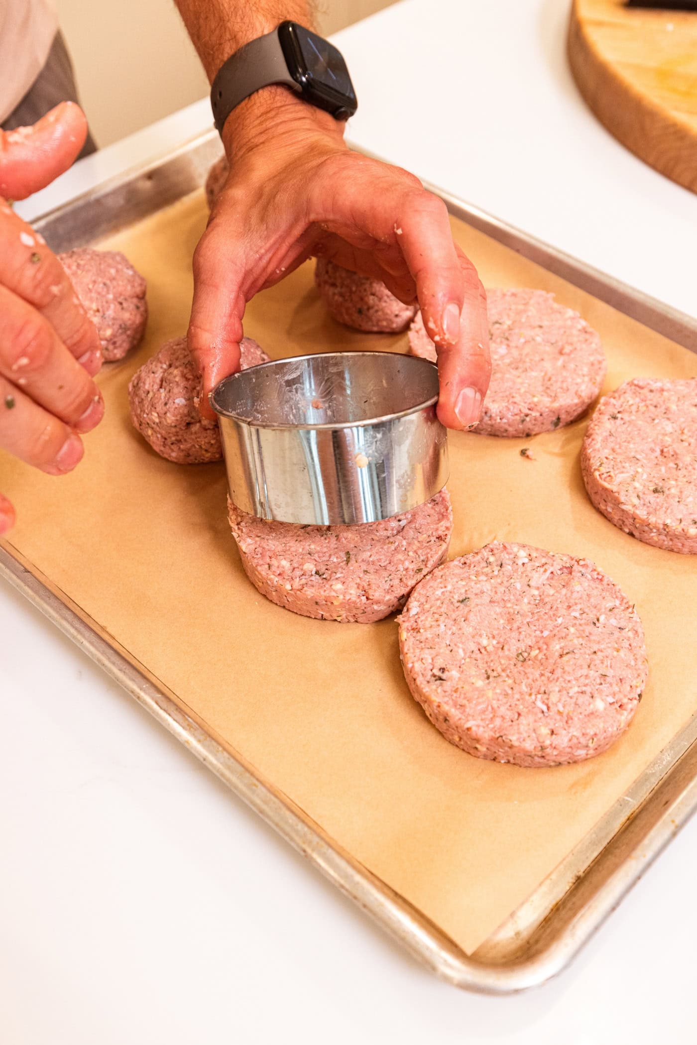 Hand using biscuit cutter to form perfect rounds for turkey burgers on parchment-lined baking sheet.