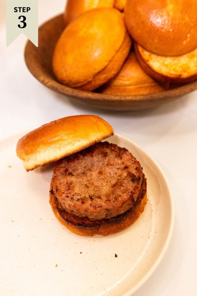 Grilled Greek turkey burger sitting on a grilled hamburger bun on a white plate.