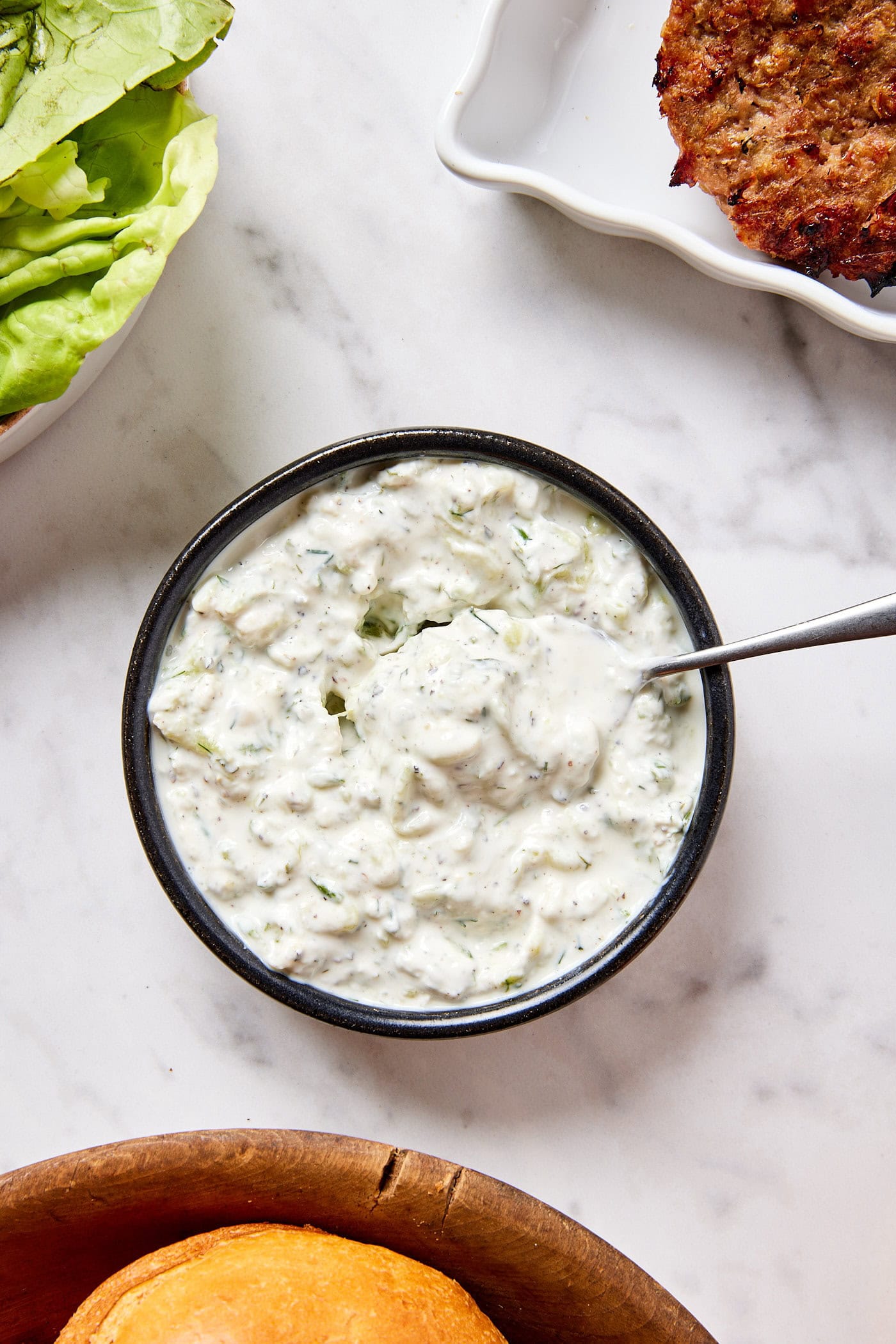 Black bowl filled with homemade tzatziki sauce with spoon resting on the side of the bowl.