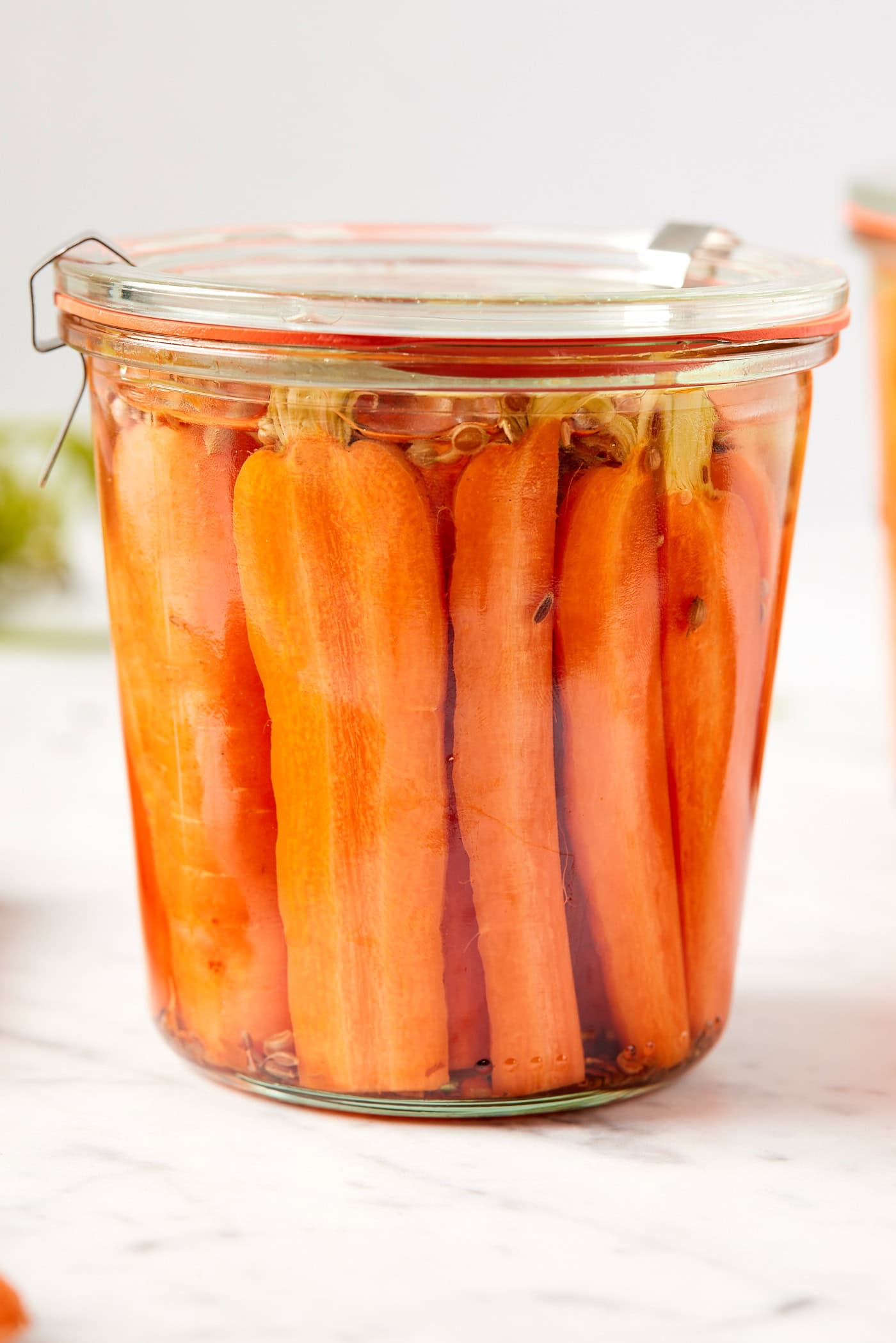 Glass jar with glass lid with quick pickled carrots inside all on white marble surface.