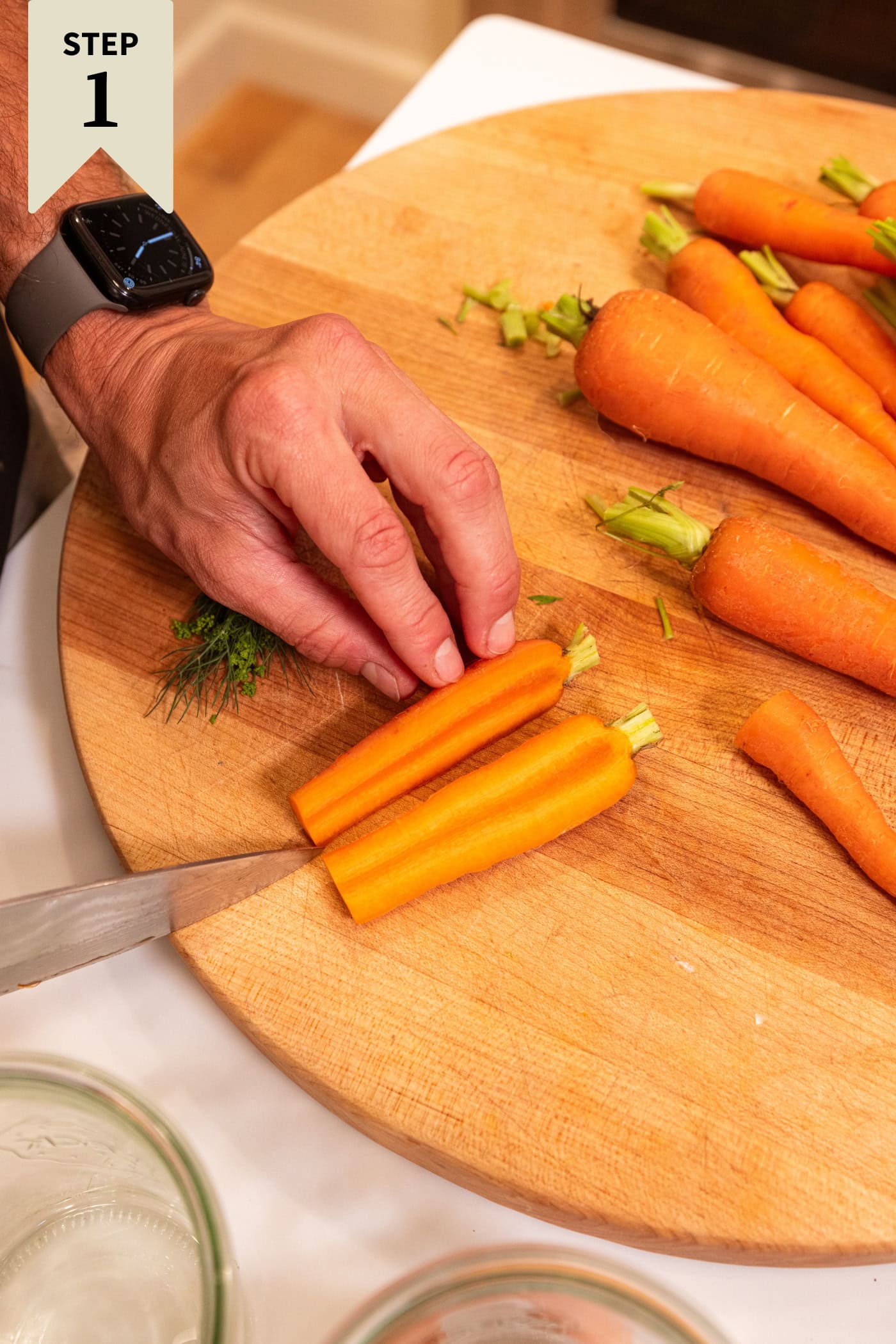 Knife slicing large carrot in half lengthwise to create carrot sticks.