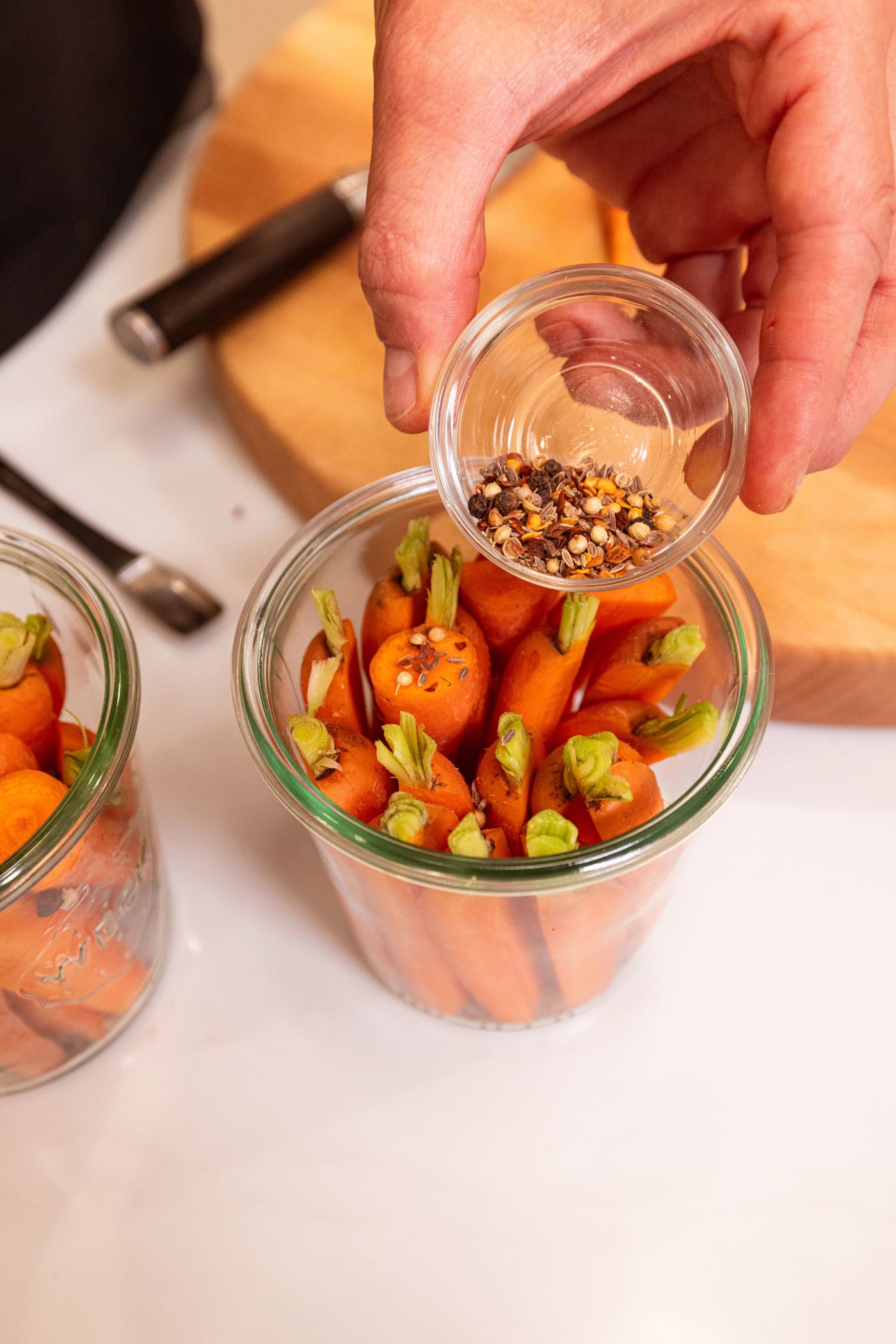Hand pouring spice mixture on top of raw carrots for quick pickled carrots.