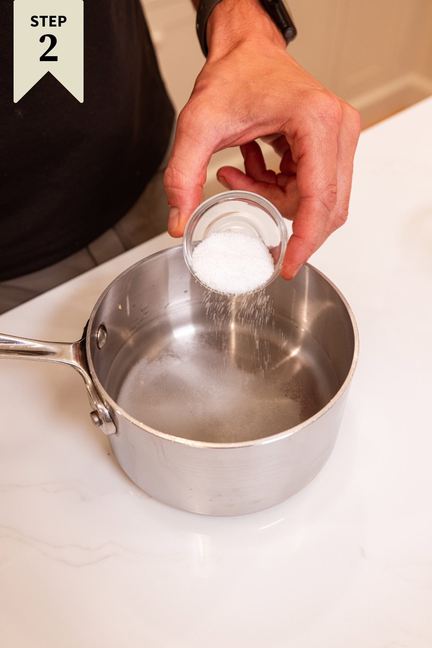 Hand holding sugar in small bowl pouring into a saucepan with vinegar and water for a pickle brine.
