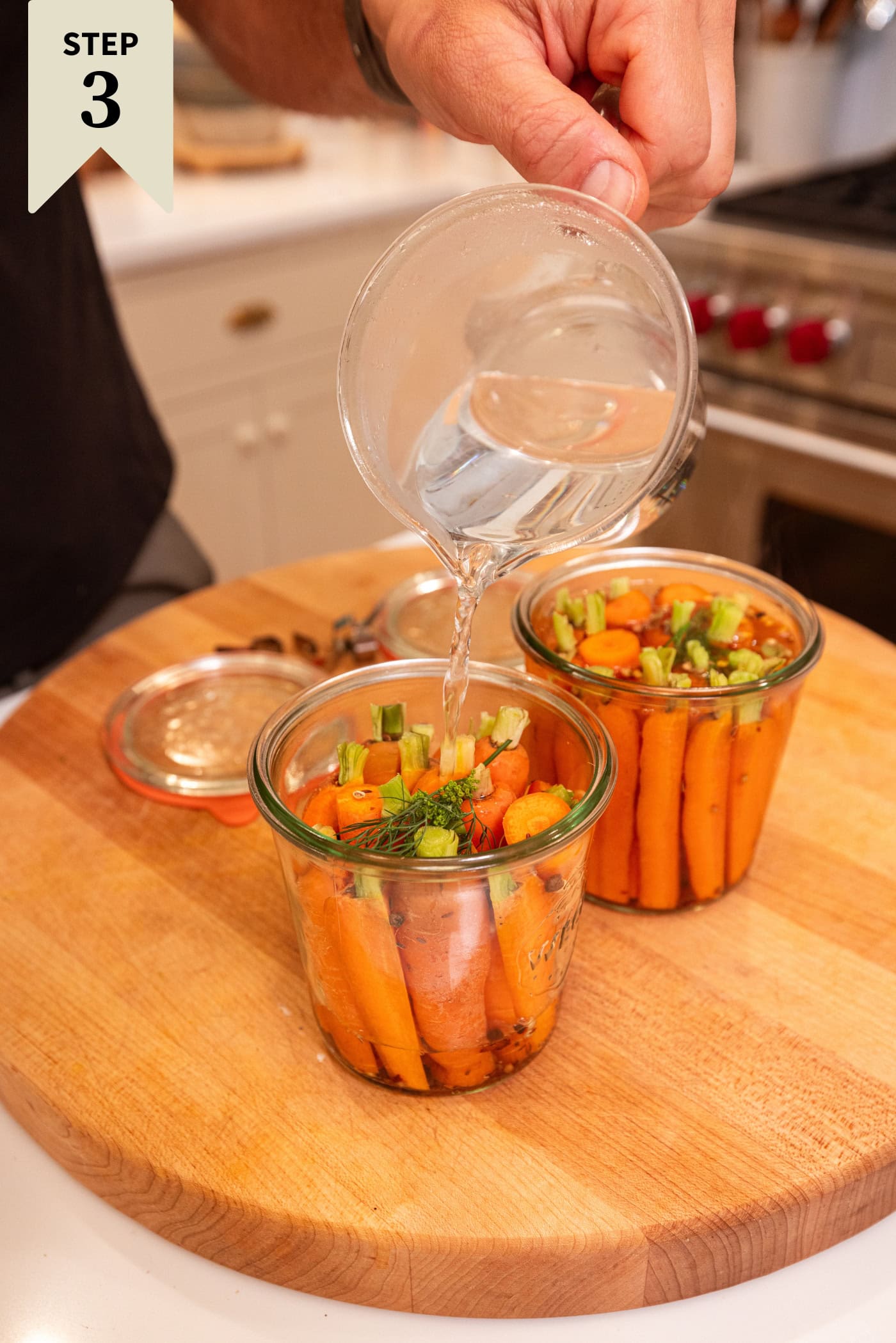Glass measuring cup pouring hot vinegar brine over the top of carrots for a quick pickle.
