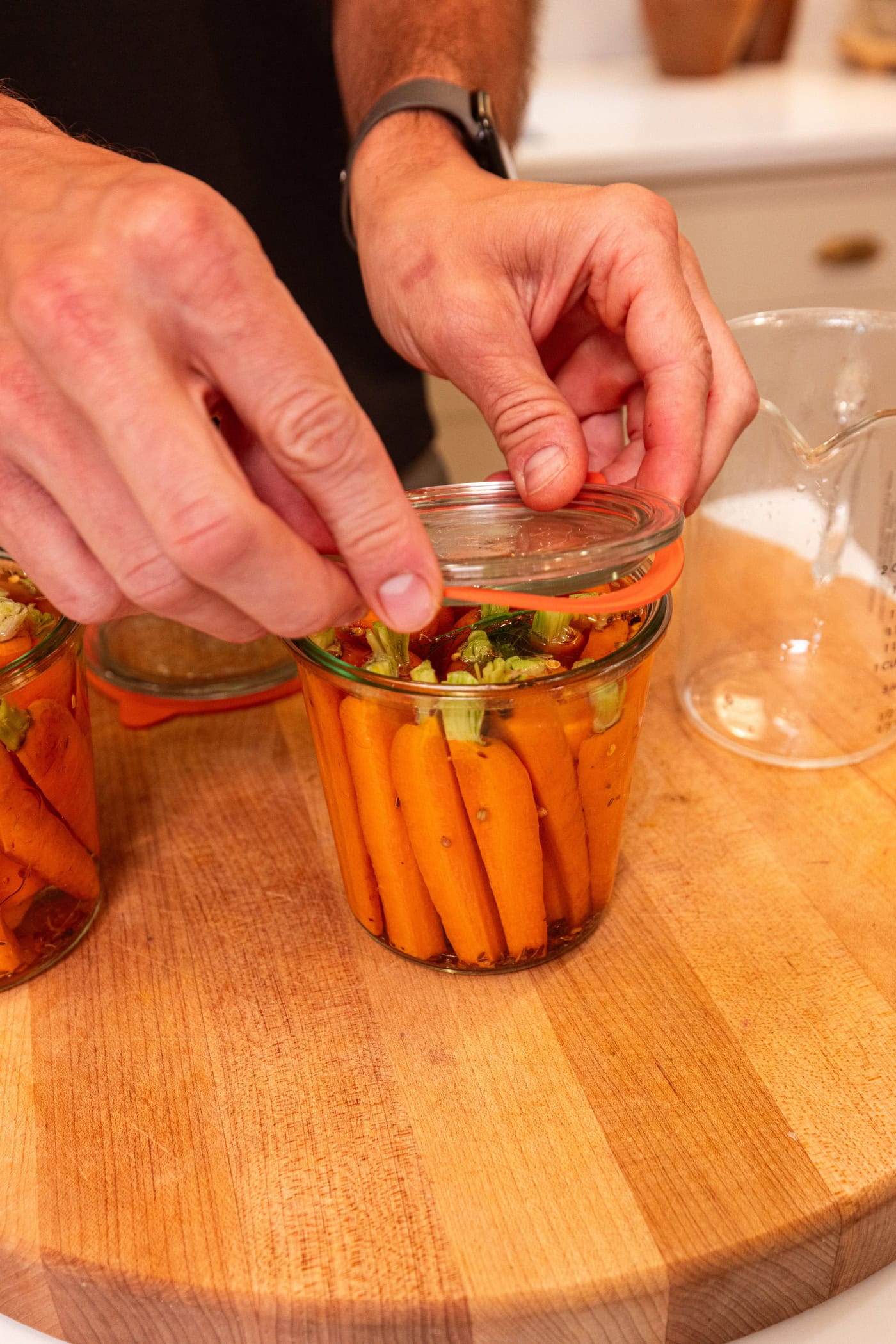 Hand placing glass lid on top of glass jar for quick pickles.