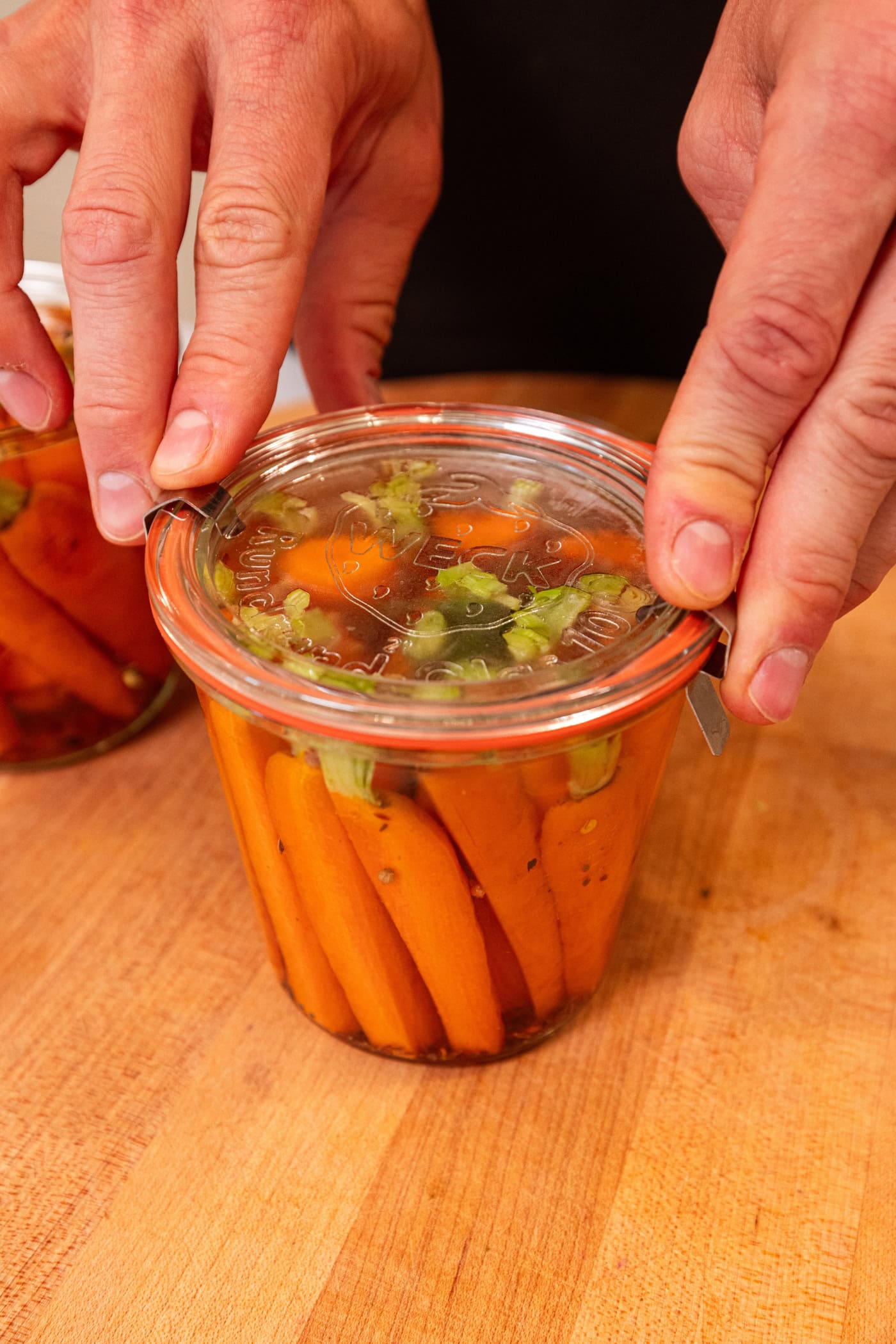 Hands snapping clasps onto glass jars filled with quick pickled carrots.