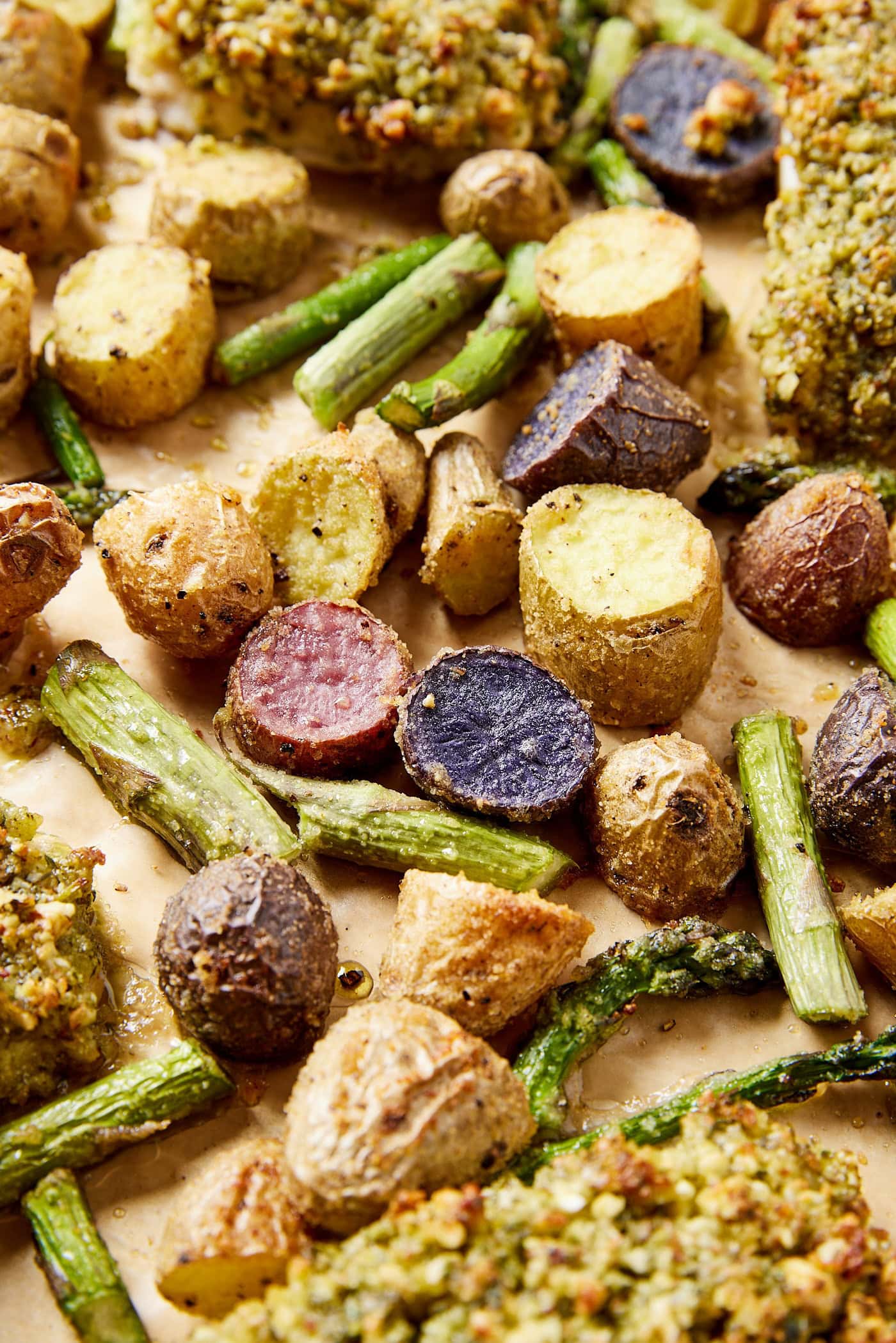 Sliced and roasted potatoes and asparagus sitting on a sheet pan after coming out of the oven with herb crusted white fish to the side.