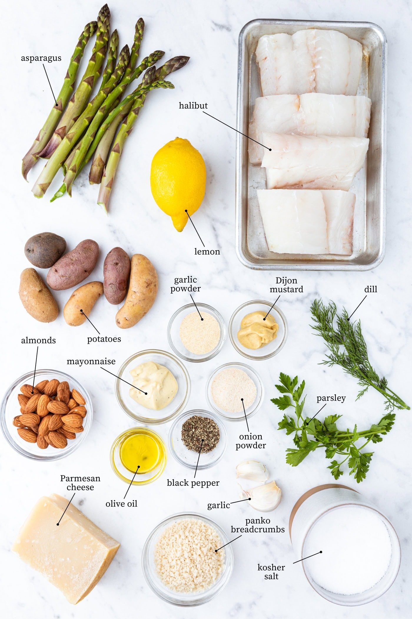 All ingredients needed for an herb crusted baked halibut meal including raw fish, lemon, asparagus, potatoes, herbs, spices, and more.