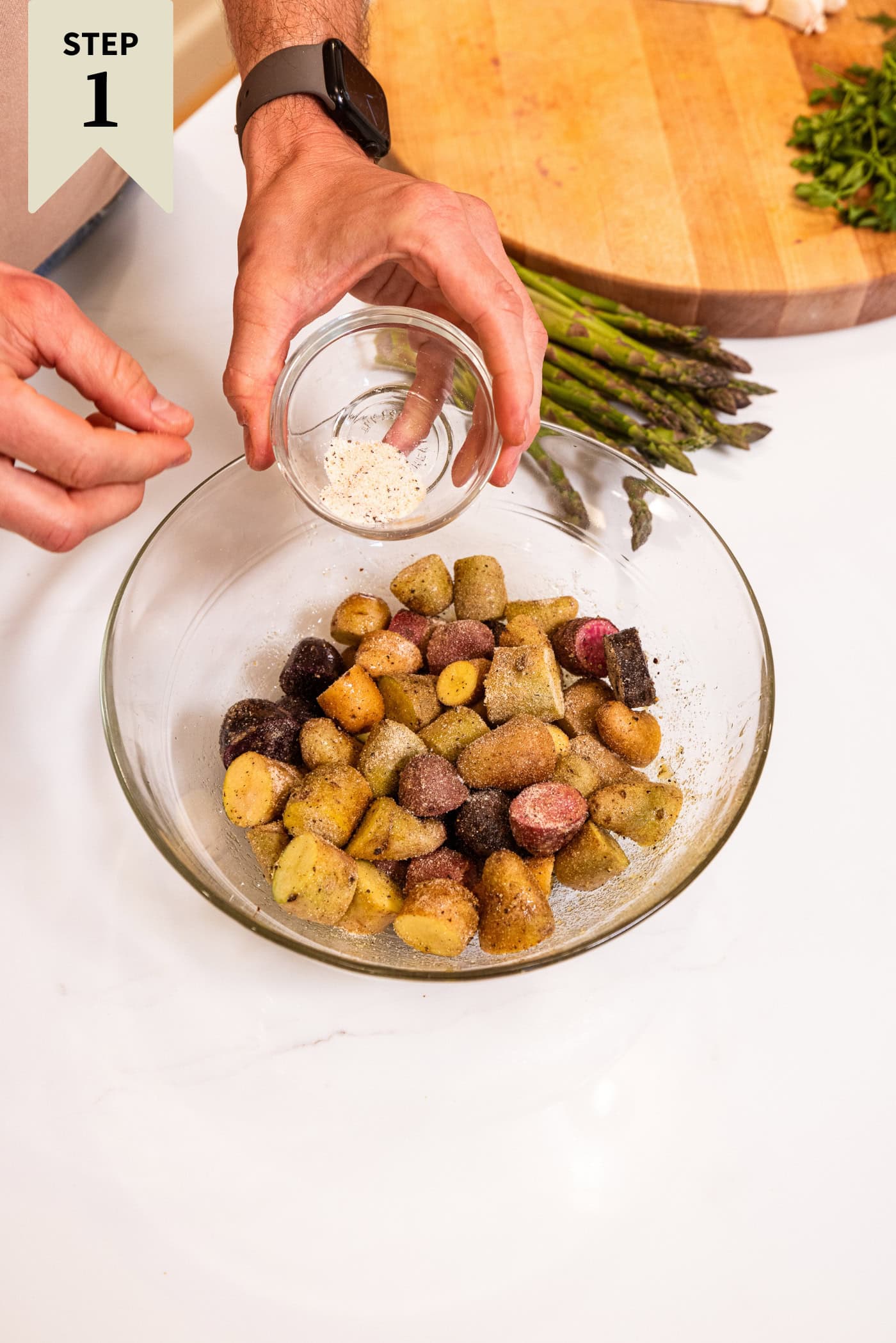 Glass bowl with sliced pieces of potato with hand sprinkling spice mixture on top.