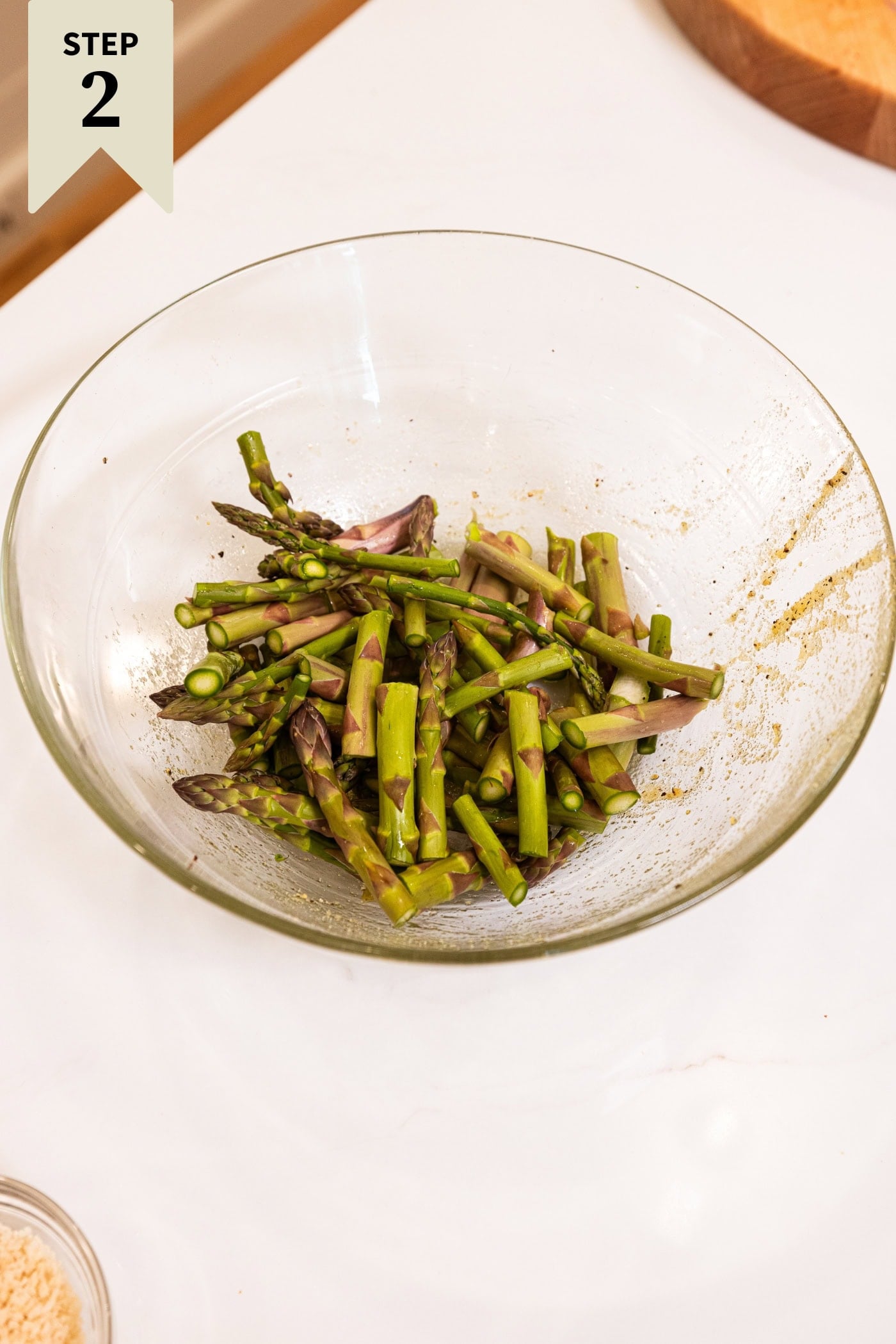 Glass bowl with sliced asparagus tossed with spices and olive oil.