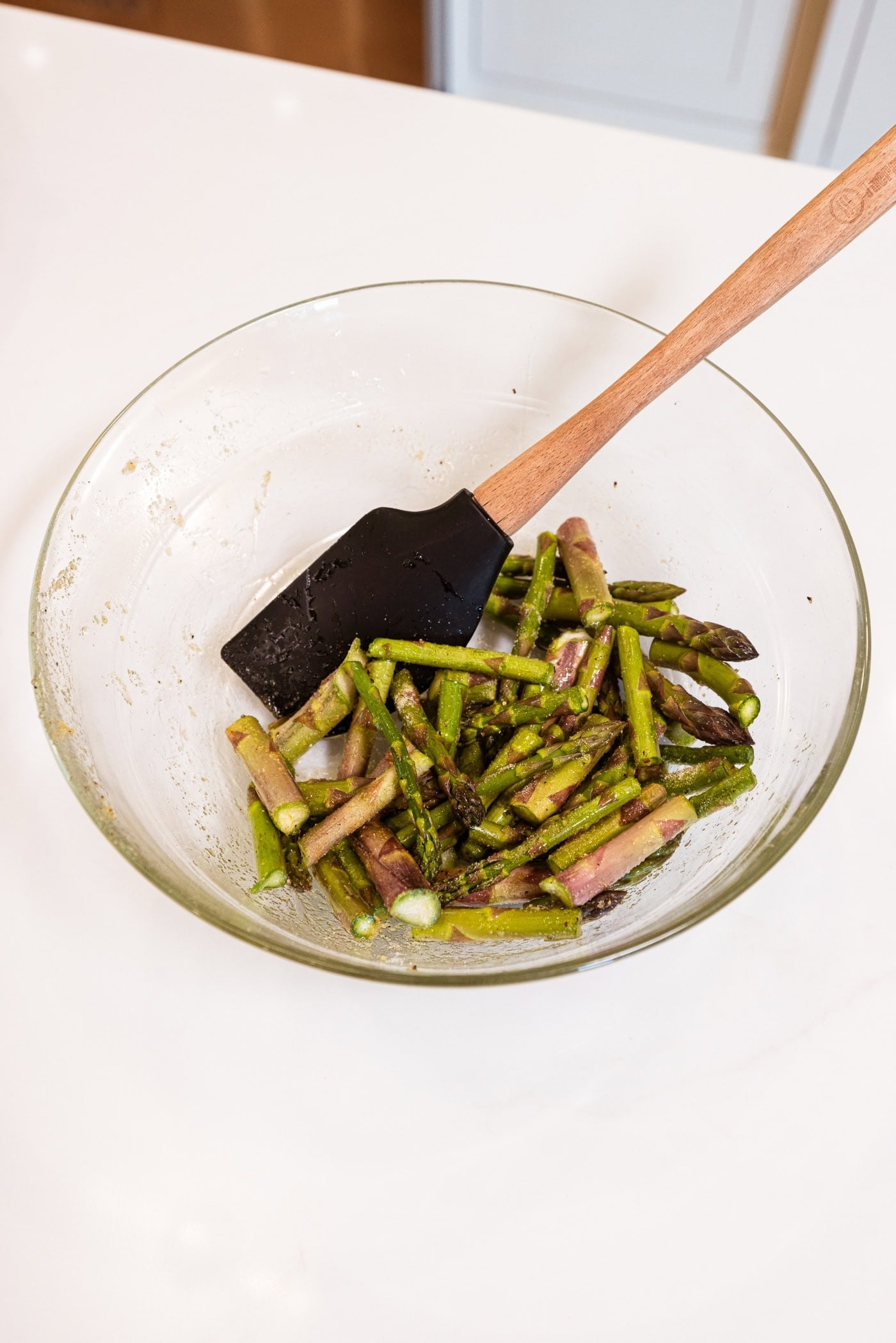 Glass bowl with spatula mixing sliced pieces of asparagus with spices.