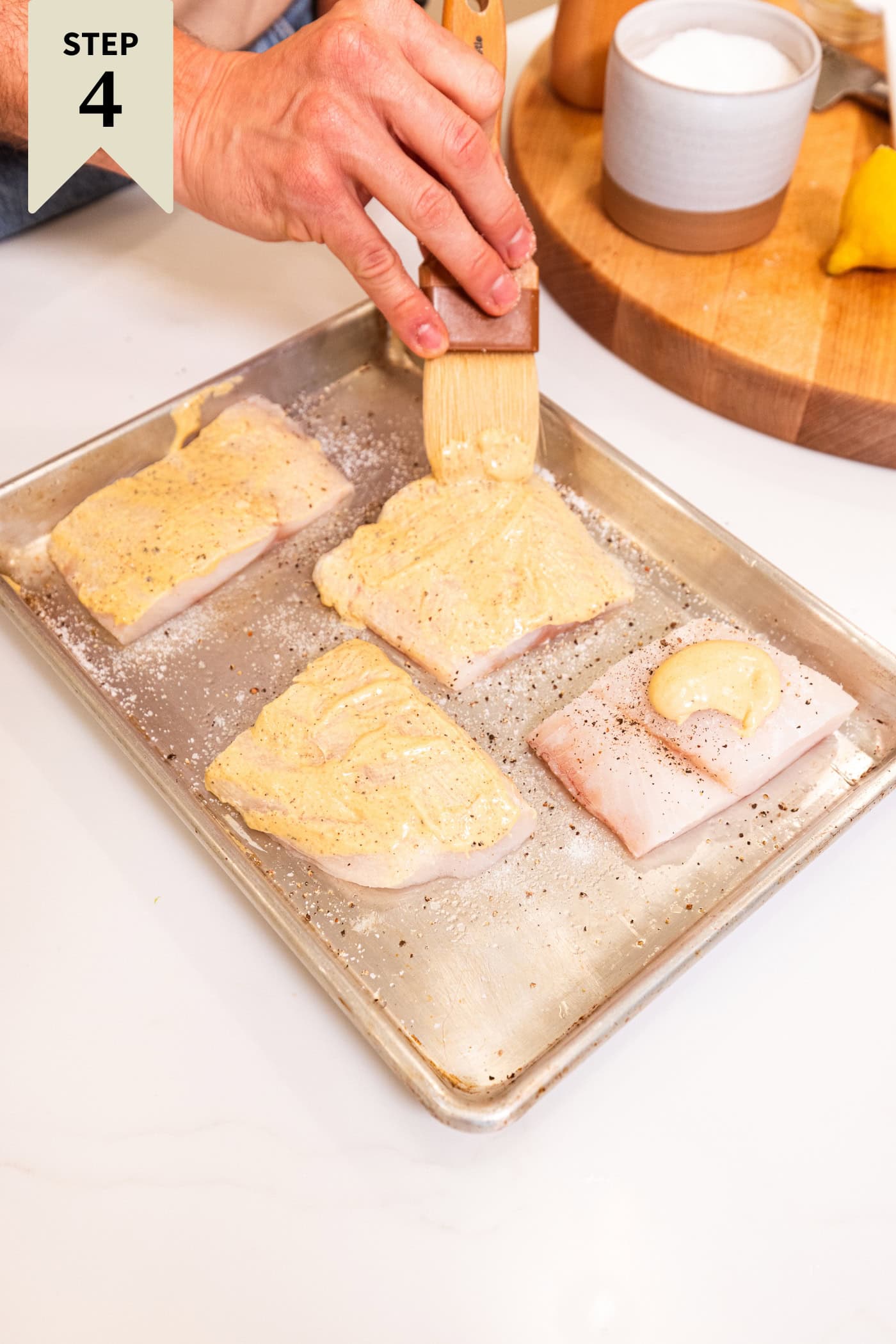 Sheet pan with pieces of halibut with mustard mixture being spread on top.