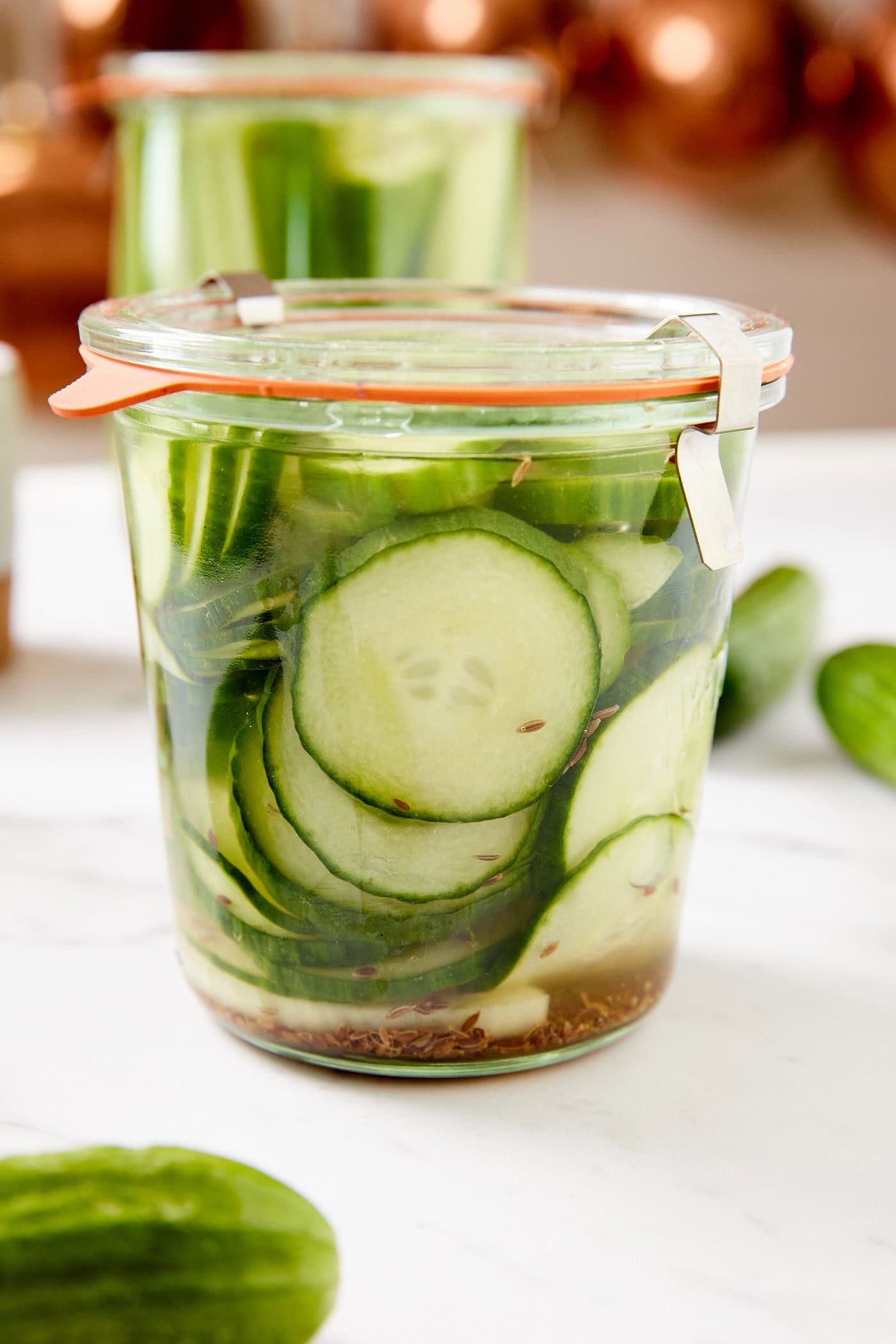 Dill pickles sitting in glass jar with brine liquid all around all on white surface.