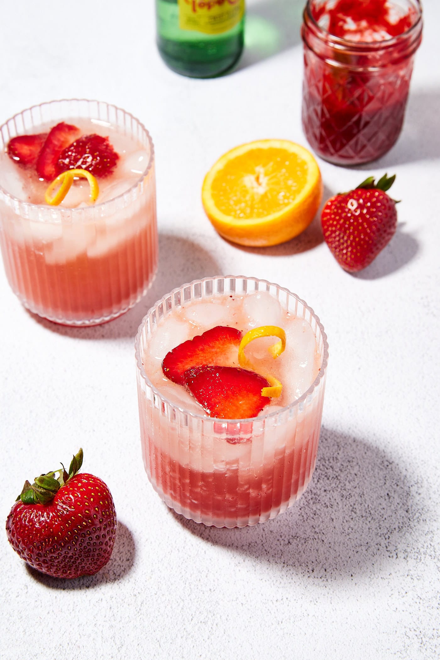 Two glasses filled with a gin spritz topped with slices of strawberry and orange peel.