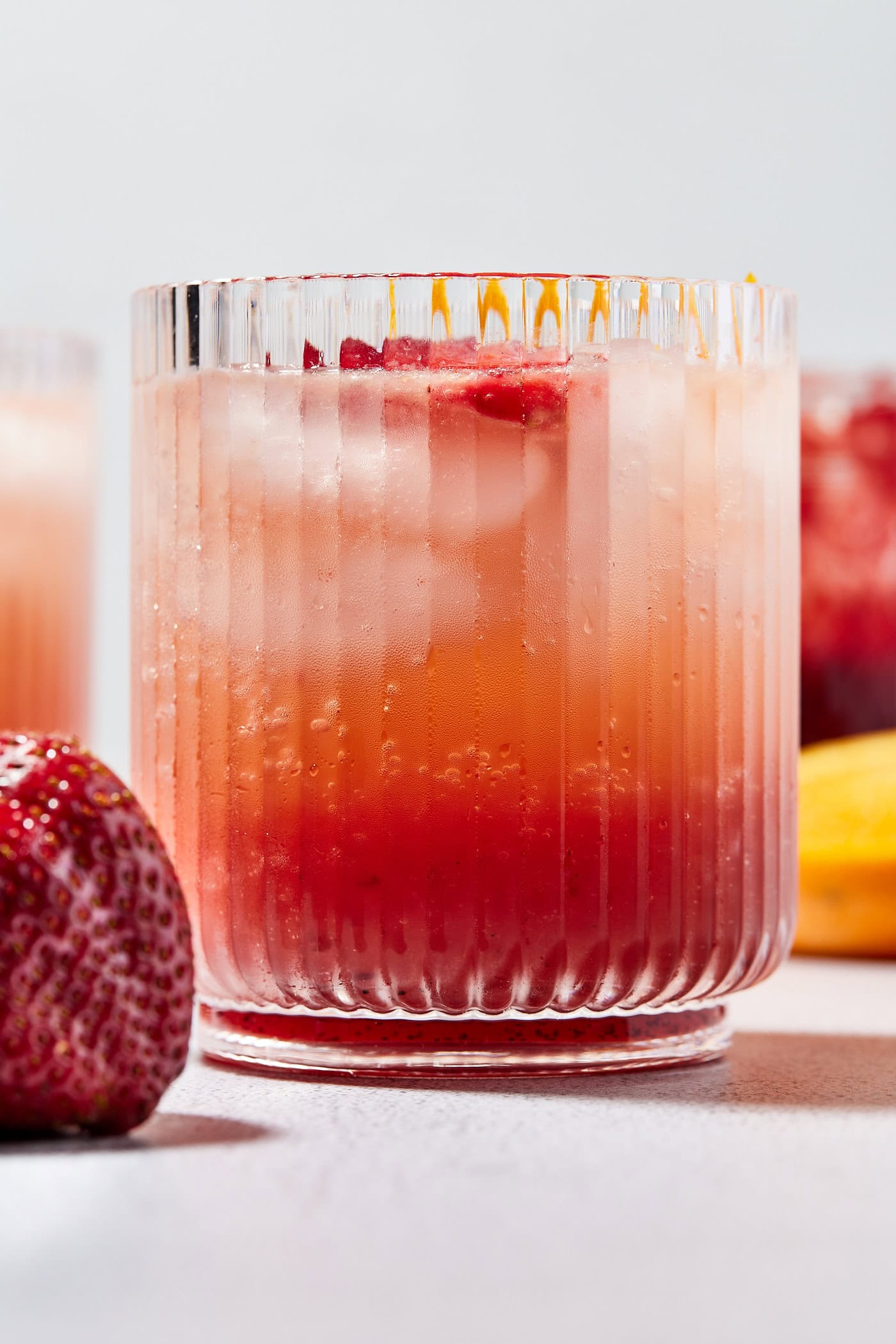 Glass with strawberry gin spritz with ice cubes and slices of strawberry with ombre red color.