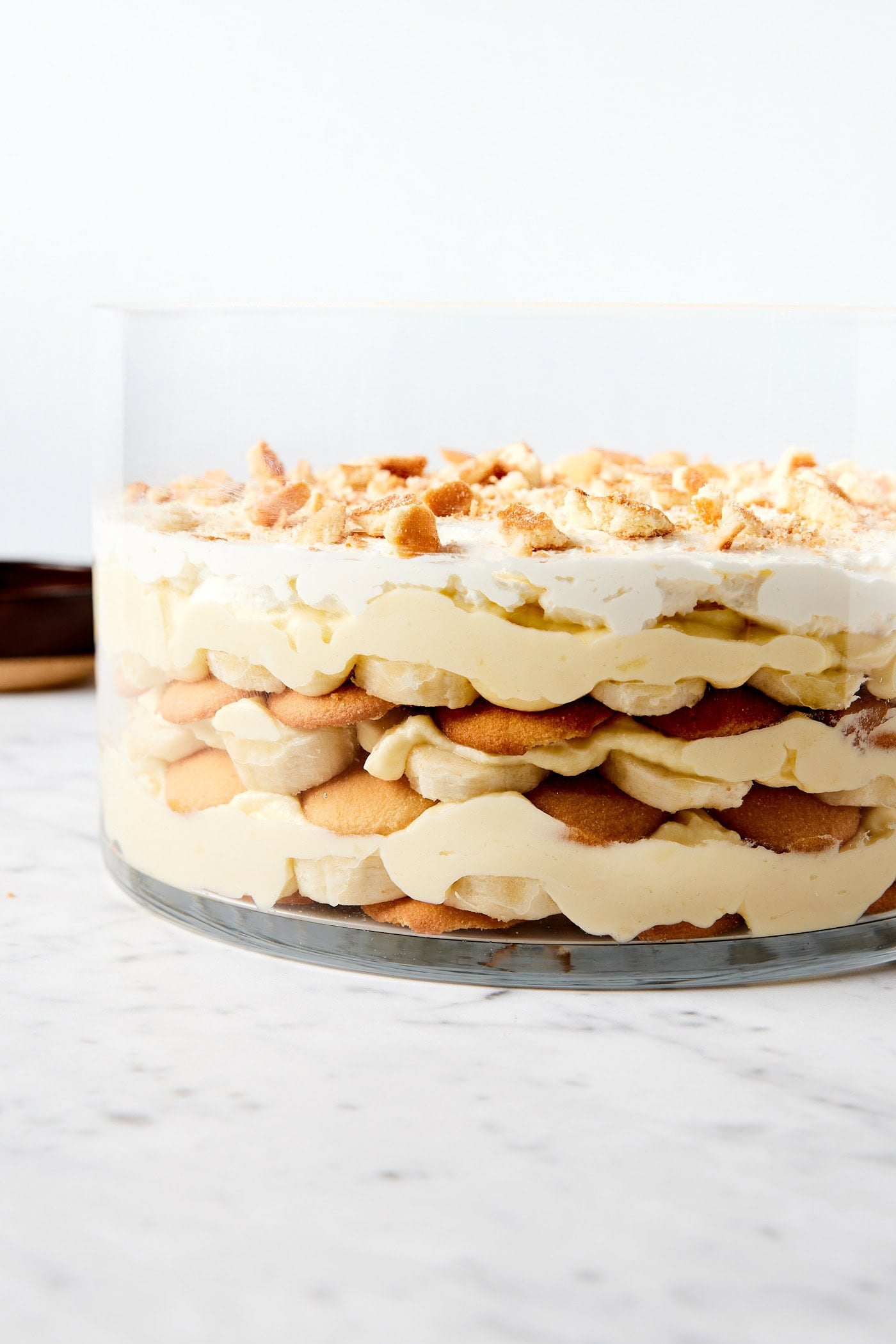 Glass trifle dish with layers of banana pudding including whipped cream, sliced bananas, vanilla wafers, and vanilla pudding.