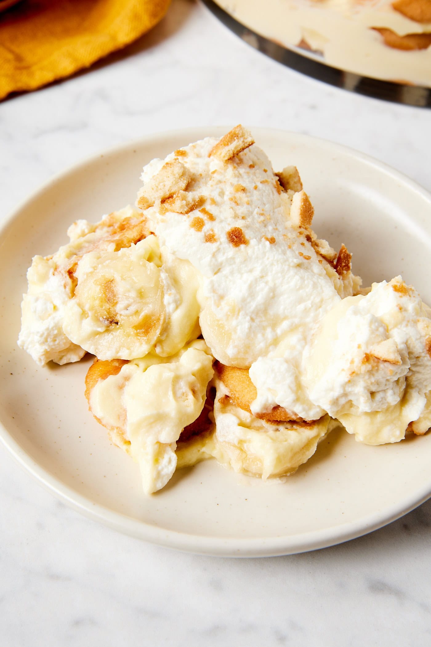 White plate filled with serving of dessert with slices of banana and whipped cream and vanilla wafers all over.