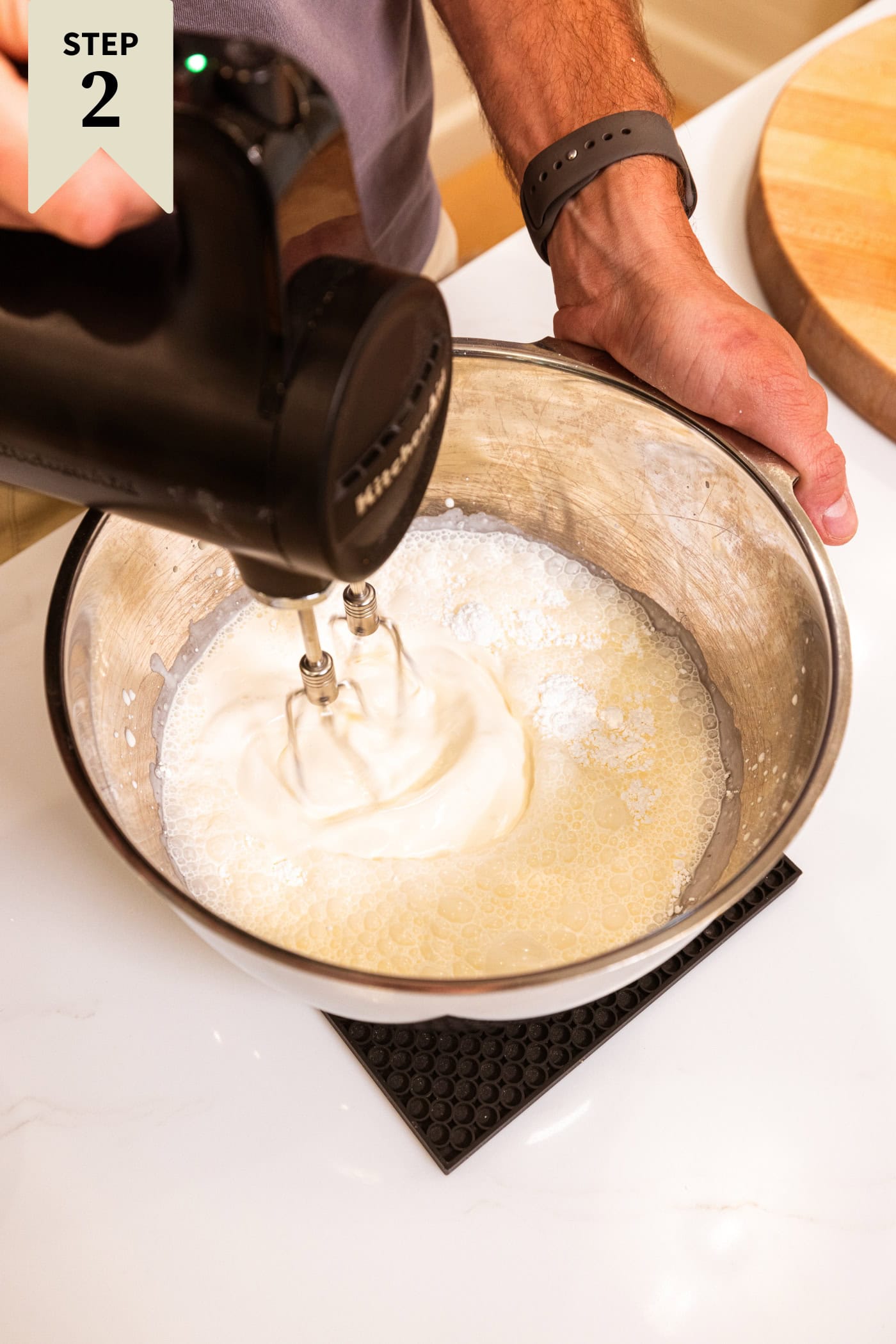 Metal bowl with electric handheld mixer making whipped cream from frothy milk.