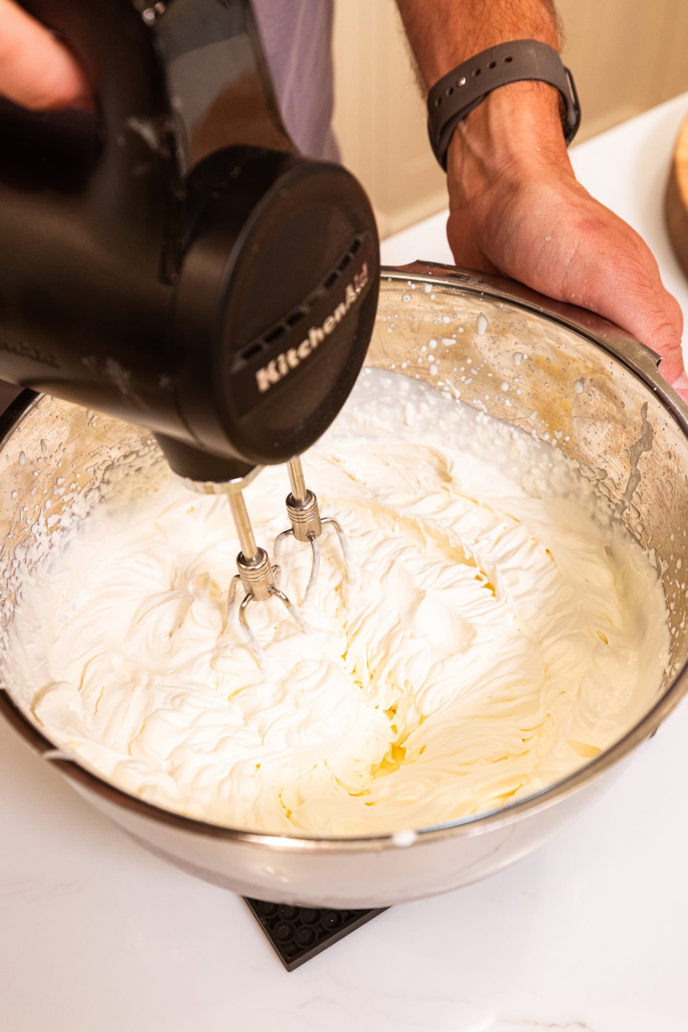 Beaters from a handheld mixer mixing together cream to form whipped cream with peaks showing.