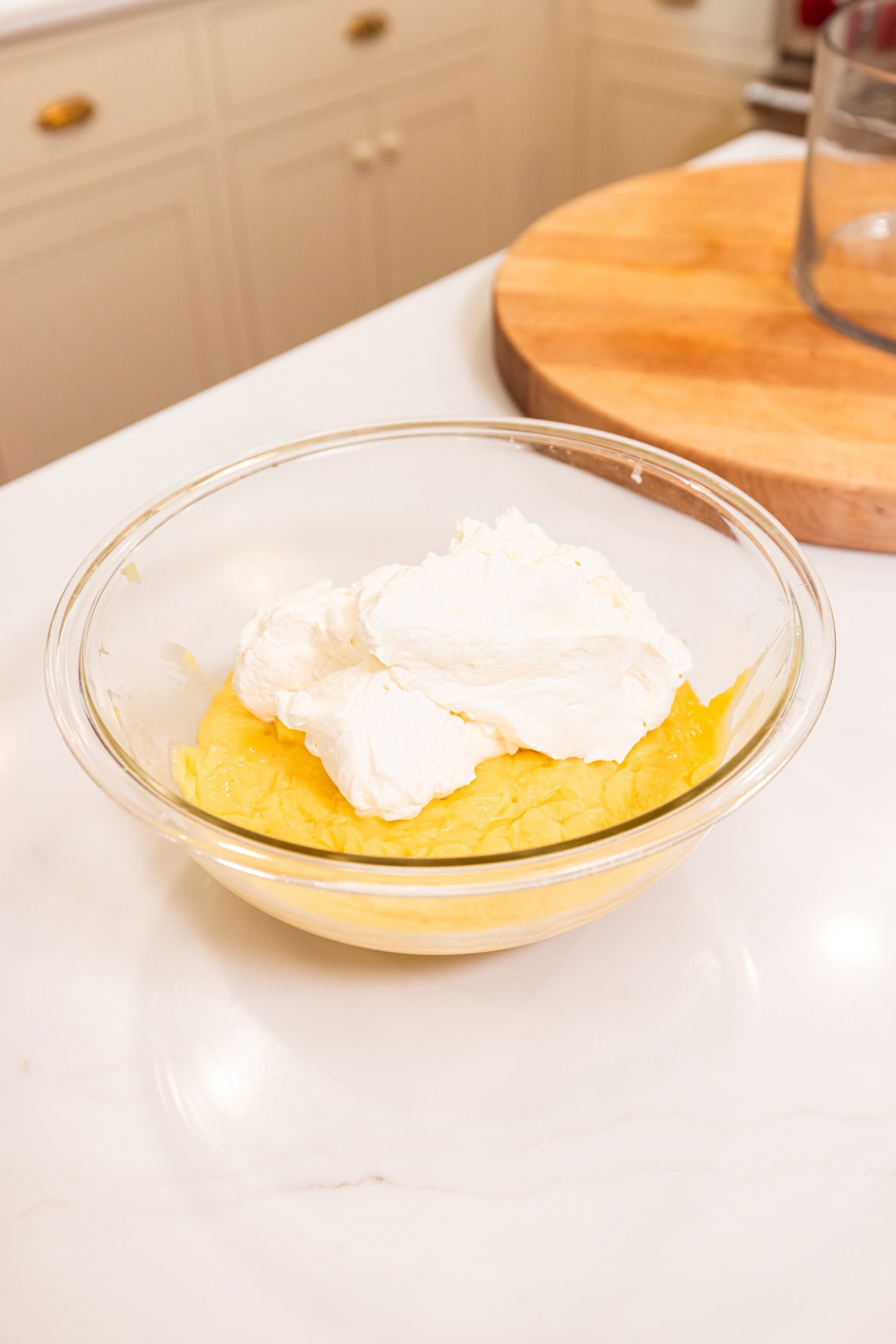 Vanilla pudding in a glass bowl with whipped cream on top before being mixed together.