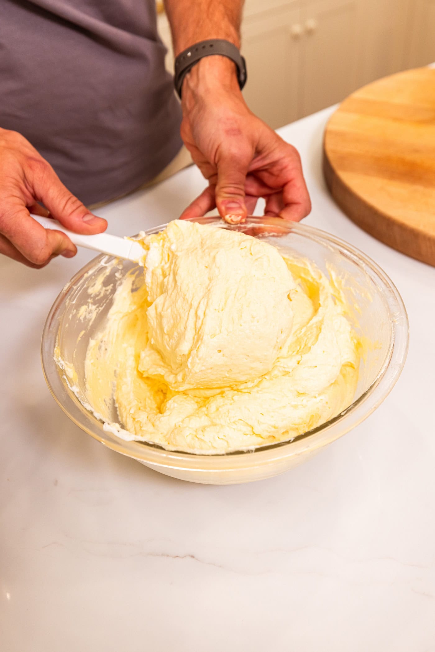 Hand using spatula to mix together whipped cream with vanilla pudding for dessert recipe.