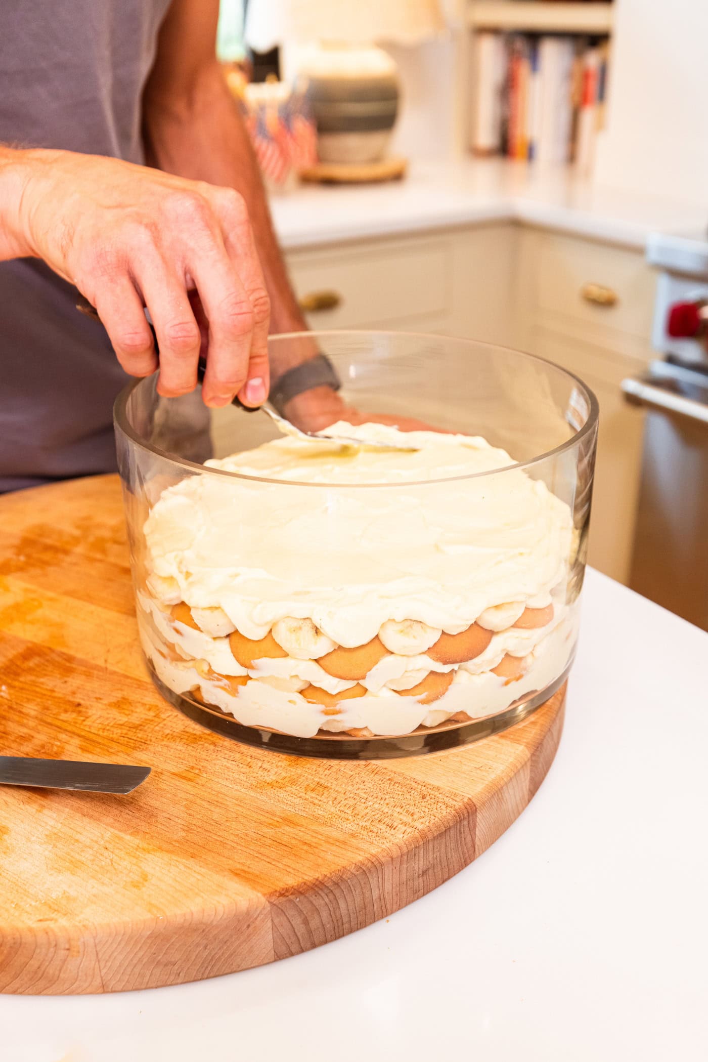 Hand sprinkling crushed vanilla wafers on top of layers of pudding and banana for banana pudding recipe.