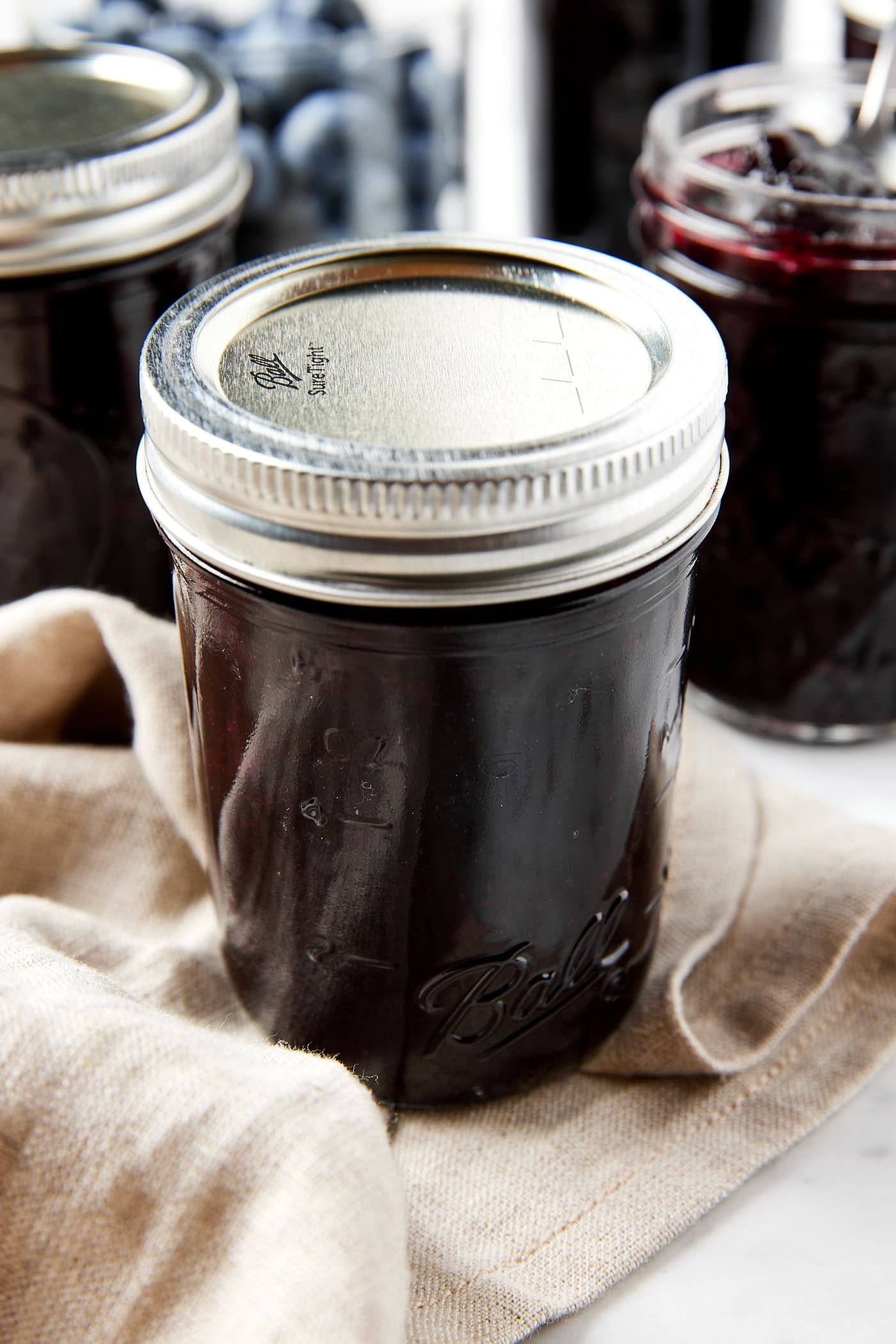 Jam jar with lid and ring on top filled with jam sitting on tan towel after being canned.