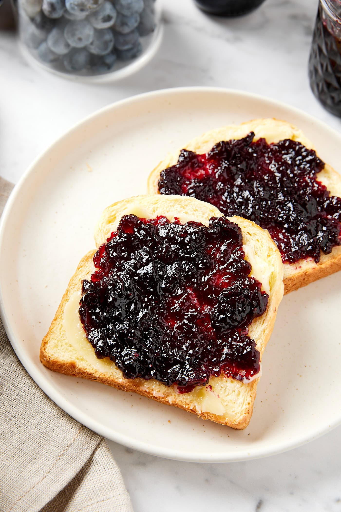 Plate with two slices of bread with butter and purple-colored blueberry jam spread on each piece.