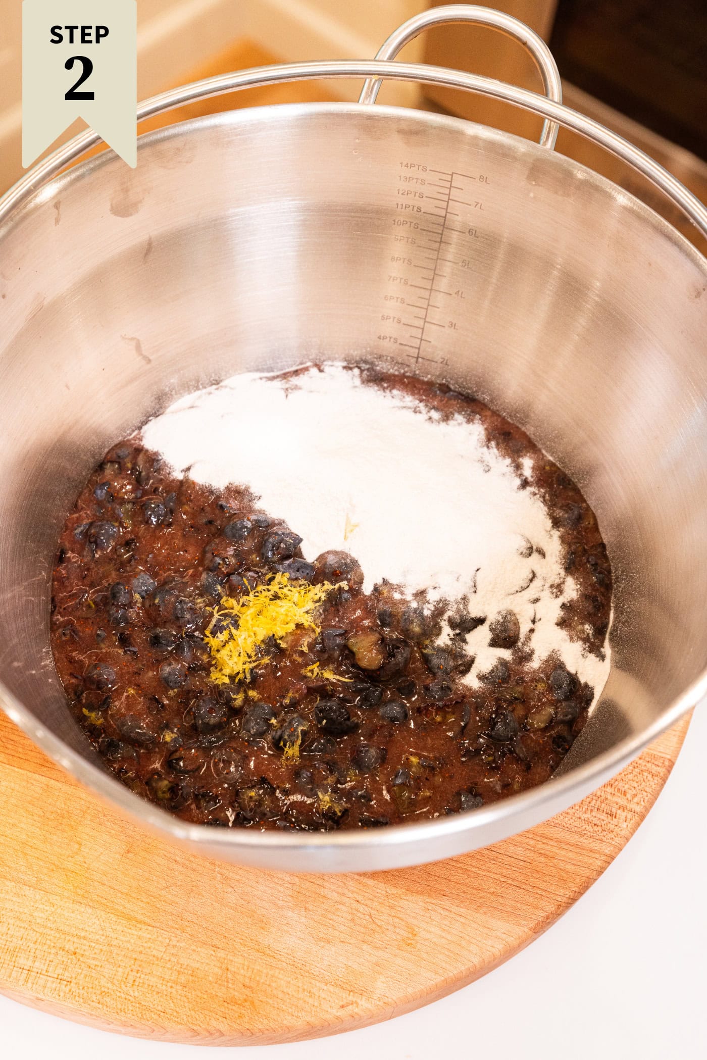 Large metal kettle filled with mashed blueberries, lemon zest, and pectin before being cooked on the stove.