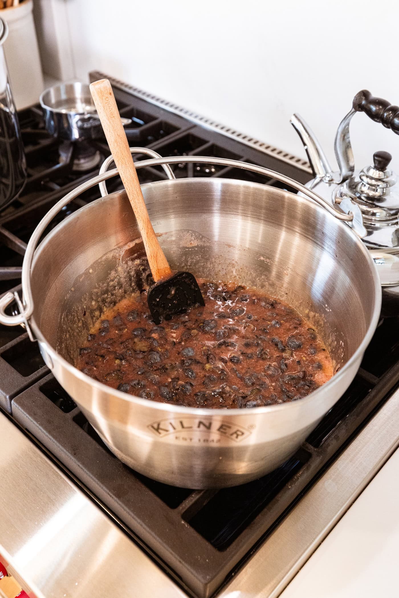 Large metal kettle with mashed blueberry mixture to make jam heating on the stovetop.