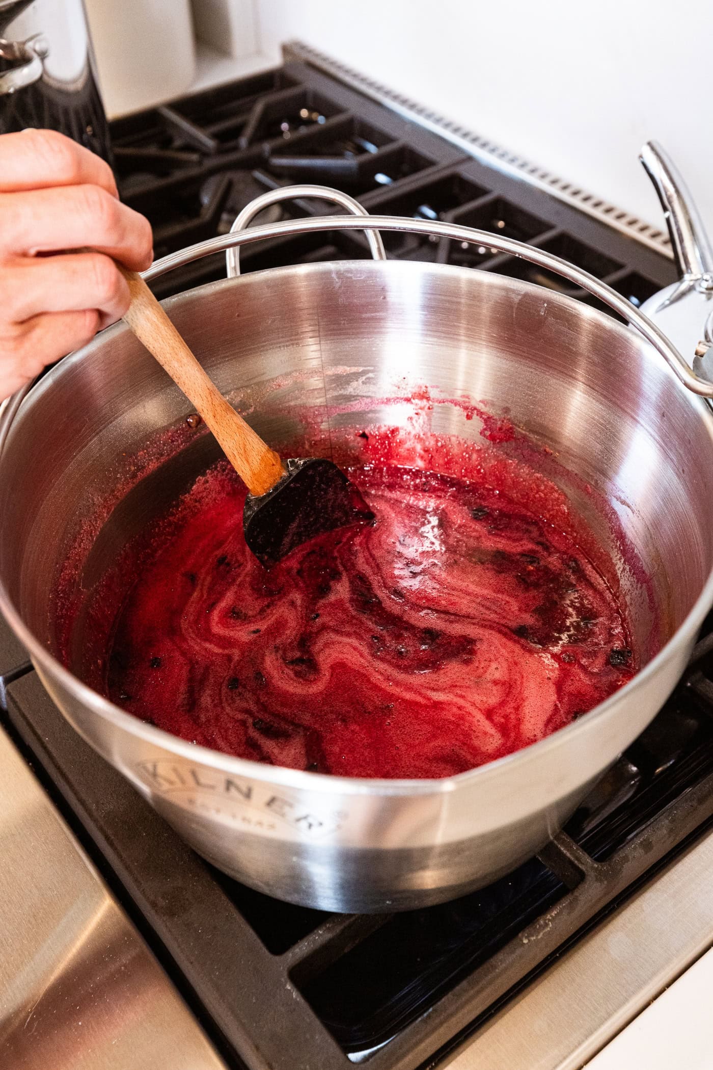 Blueberry jam cooking in a large metal pot on the stovetop with foam mixture on top.