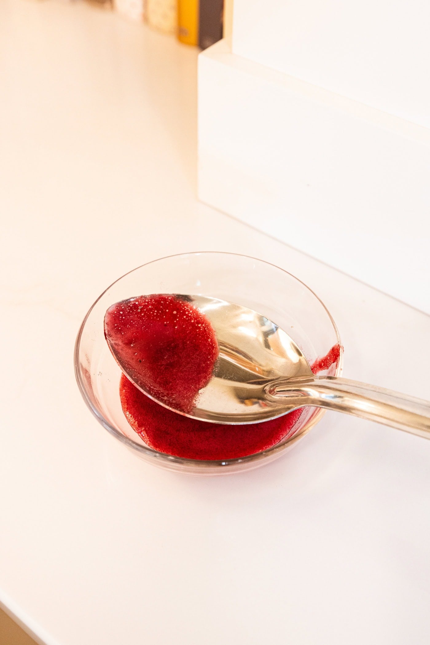 Spoon resting in small glass bowl with foam being removed from mixture being cooked on the stove.