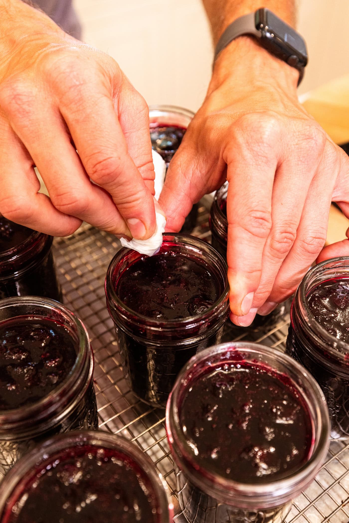 Hand wiping lid of jam jar with piece of paper towel to ensure there are no drips of jam.