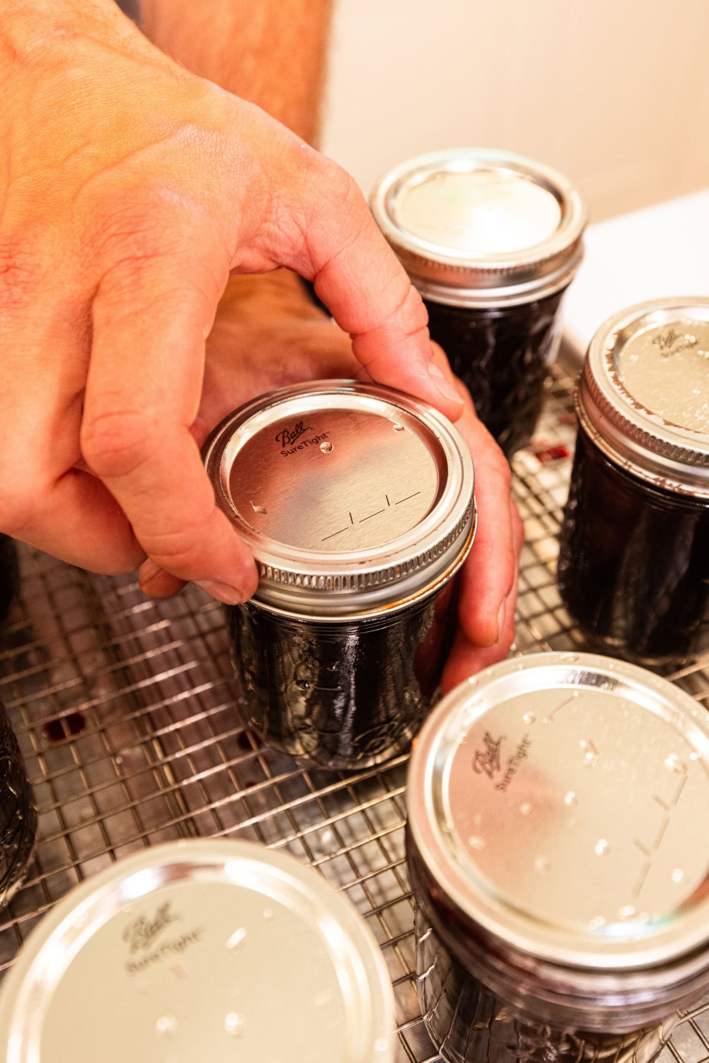 Hand twisting a lid and ring onto a jam jar before being put into the water bath canner.