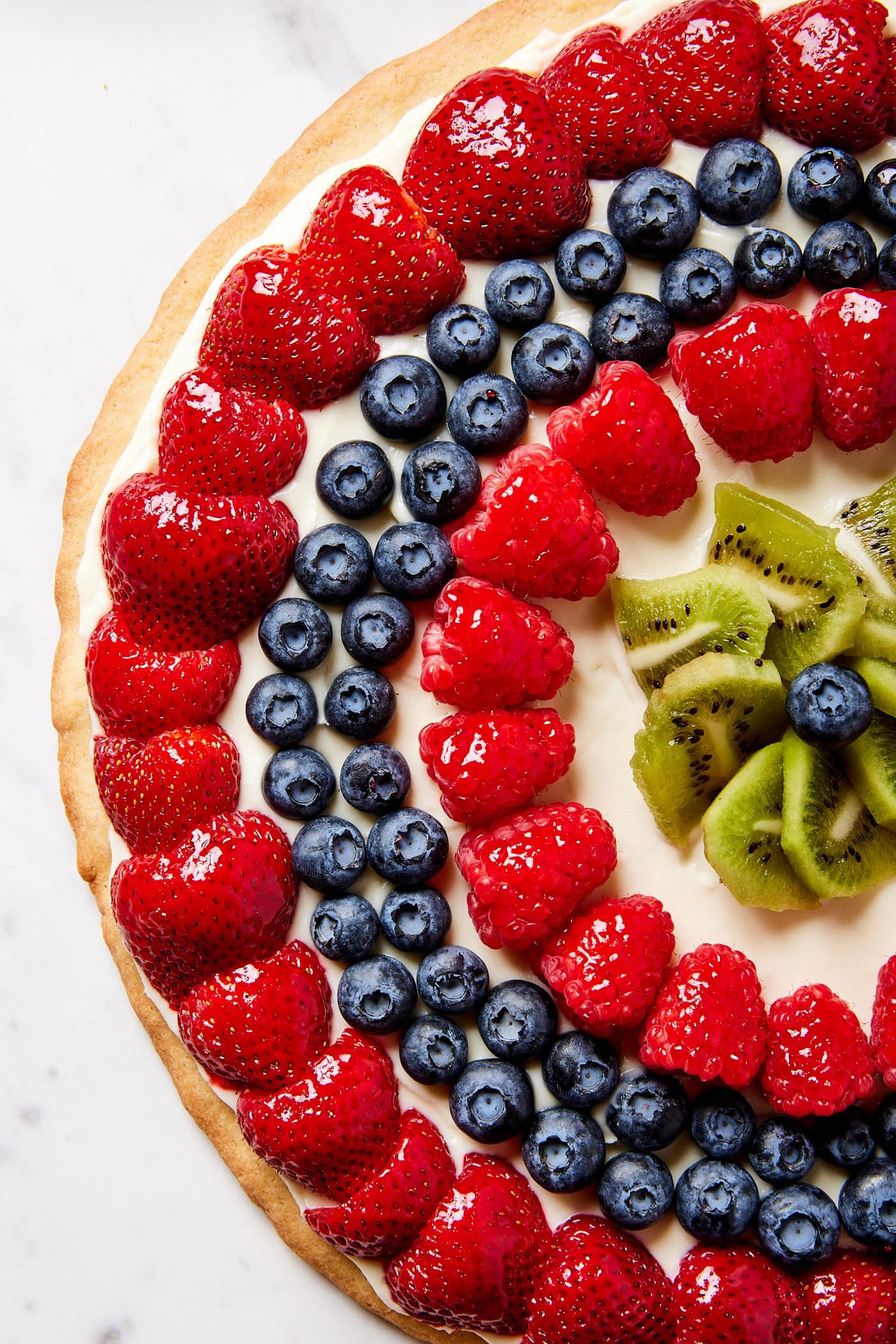 Round circles of fruit on top of dessert pizza with kiwi in the center with cream cheese frosting underneath.