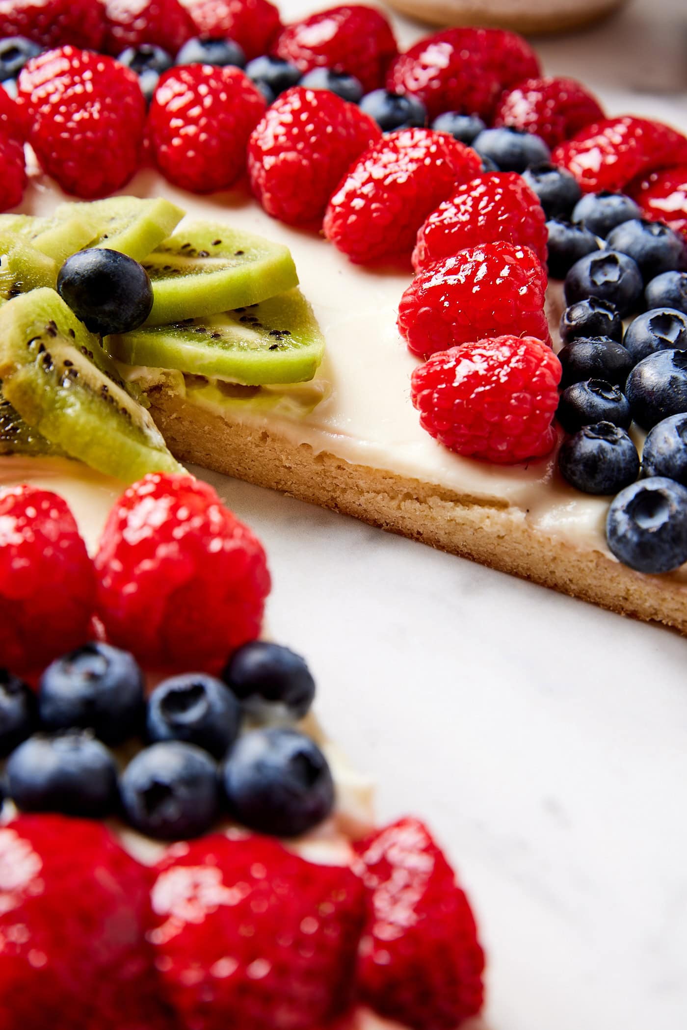 Slice of fruit pizza removed showing the interior texture of the sugar cookie crust with fruit on top.