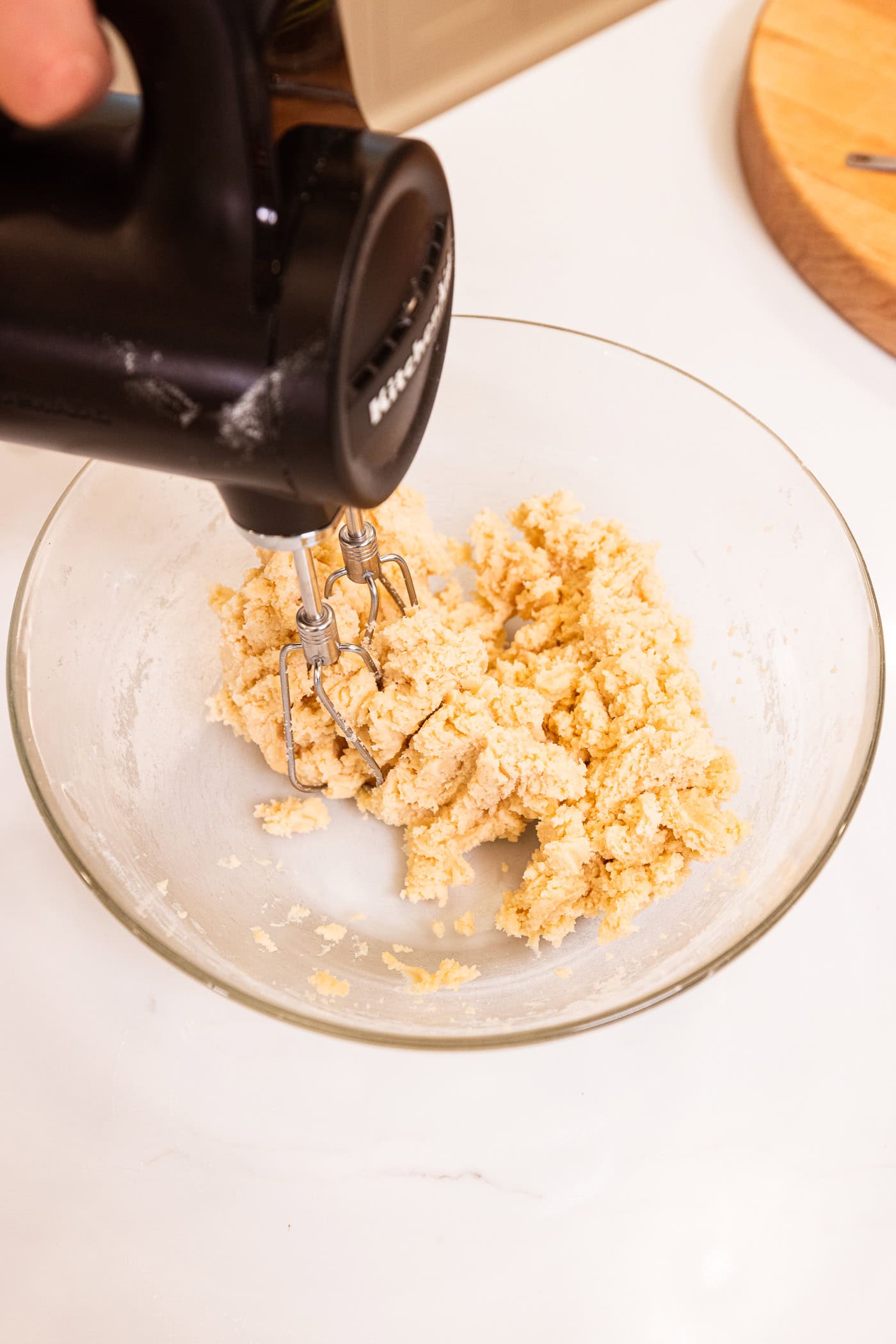 Glass mixing bowl filled with dough ingredients after being mixed together with hand mixer.