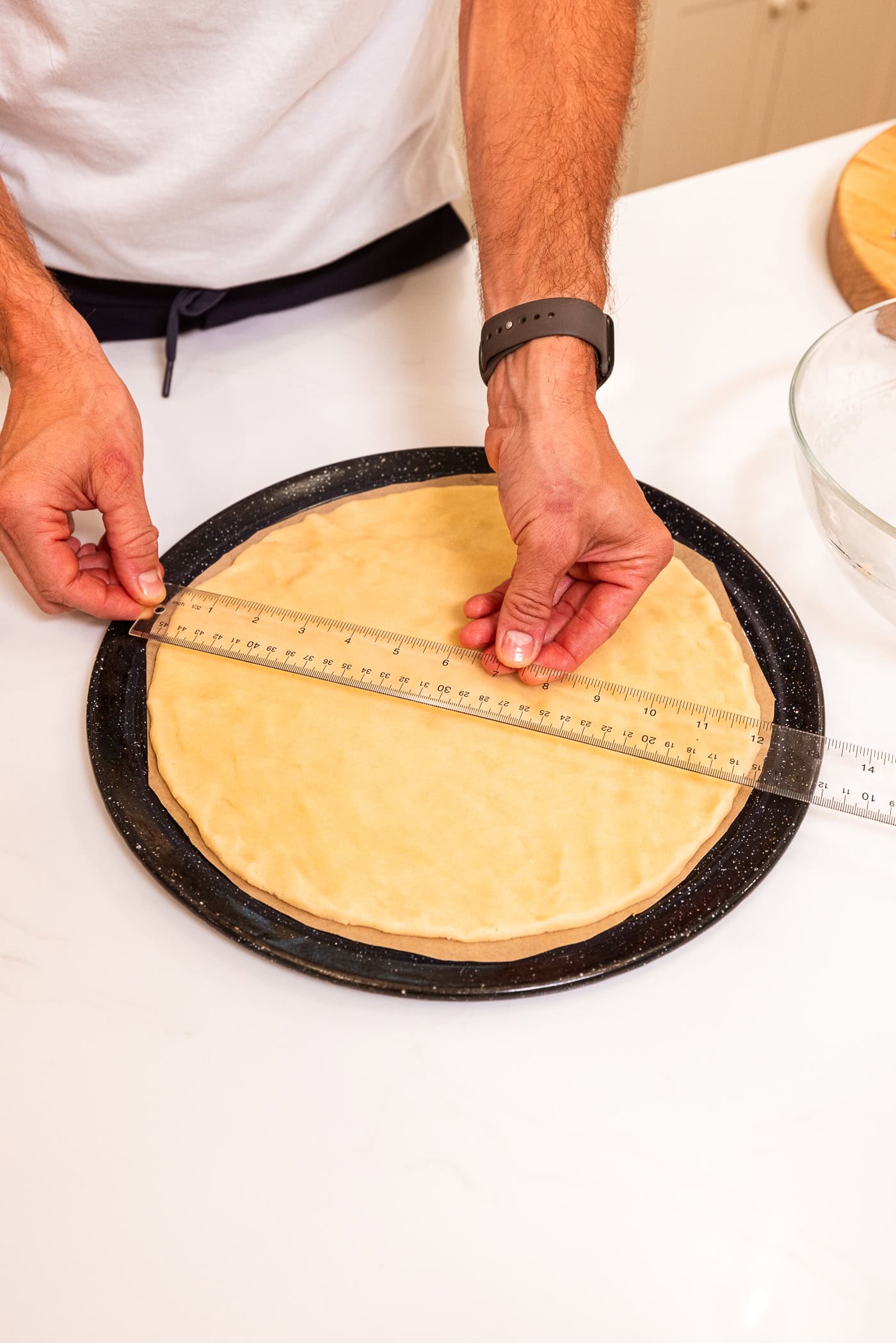 Hand using measuring tape to measure the width of a sugar cookie crust for a fruit pizza dough.