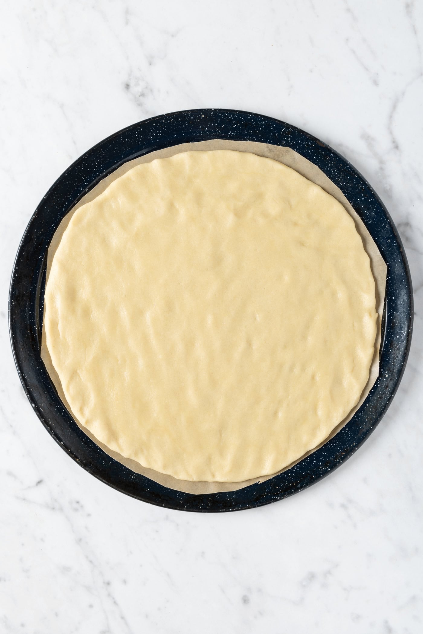 Round unbaked sugar cookie crust shaped into a circle on a pizza pan.